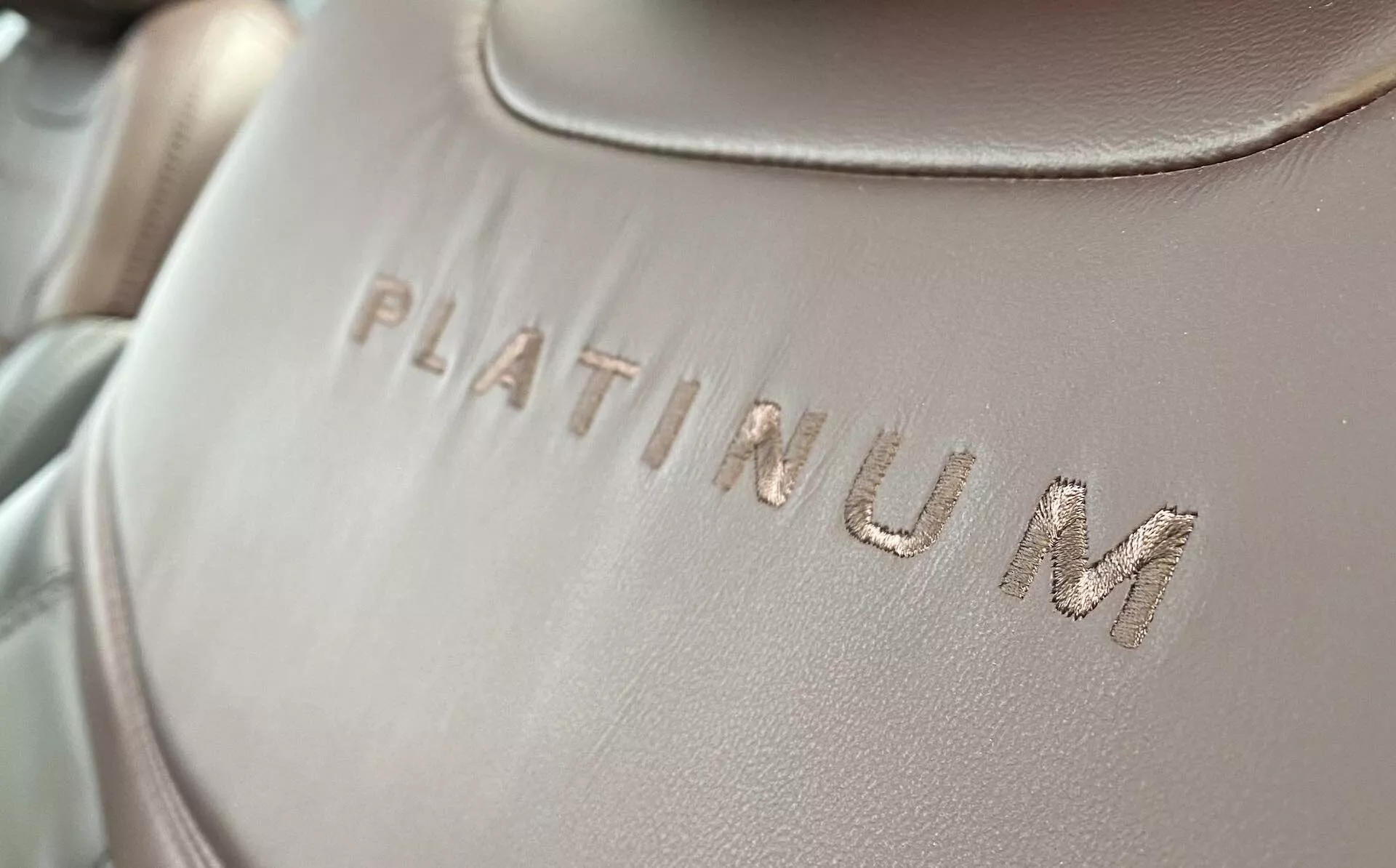 Detailný záber na interiérové čalúnenie Fordu Explorer 2019, s vyrazeným slovom 'PLATINUM' na hladkom povrchu látky alebo kože, s miernym diagonálnym uhlom. Text je zaostrený, s jemným, rovnomerne rozloženým osvetlením a malou hĺbkou ostrosti.