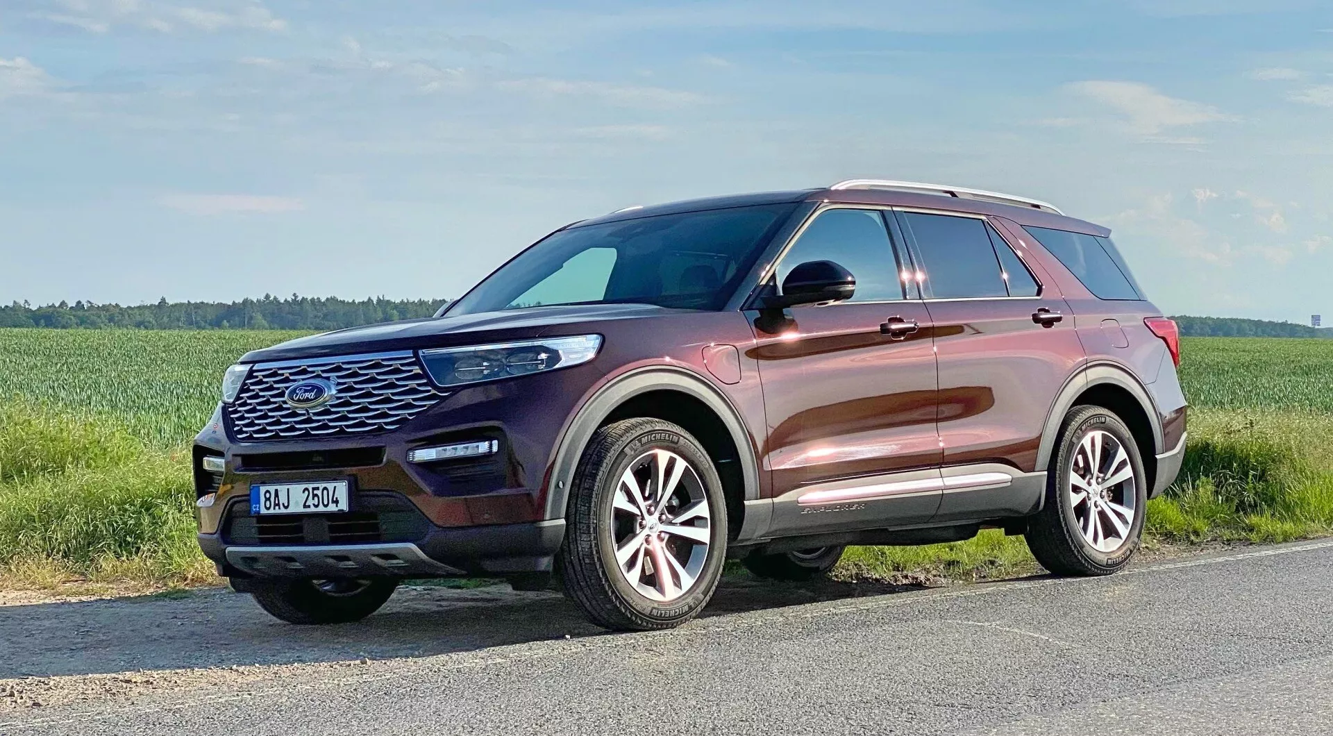 Ford Explorer 2019 - Moderné SUV zachytené z trojštvrťového čelného pohľadu, zvýrazňujúce prednú masku s šesťhranným vzorom a veľkým emblémom, kontúrovanú kapotu, elegantné LED svetlomety, hmlové svetlá, vstupné vetracie otvory, viaclúčové zliatinové kolesá, mierne stúpajúcu líniu okien, strešné nosiče, bočné zrkadlá s integrovanými smerovými svetlami a metalickú farbu karosérie odrážajúcu vysokokvalitnú povrchovú úpravu.
