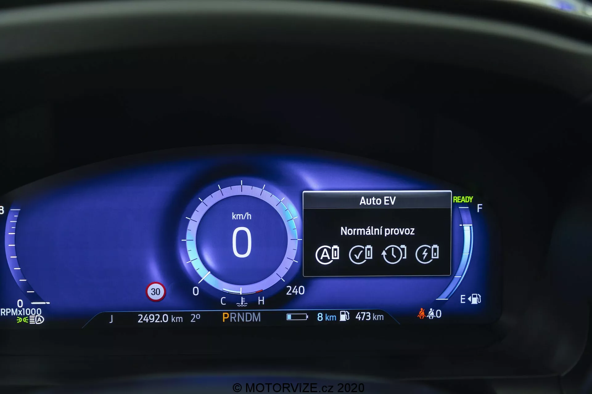 Zblízka pohľad na digitálny prístrojový panel Ford Explorer 2019 z pohľadu vodiča. Digitálny rýchlomer ukazuje 0 km/h a prístrojový panel obsahuje režim 'Auto EV', čo naznačuje elektrický alebo hybridný pohonný systém, stav 'Ready', ikony pre automatické jazdné funkcie, počítadlo najazdených kilometrov na 24 920 km, indikátor prevodovky PRNDM, stavové ikony pre batériu a vonkajšie osvetlenie, displej spotreby paliva s 8 km zostávajúcimi a maximálnym dojazdom 473 km, digitálny ukazovateľ paliva a žiadne výstražné svetlá. Modrá farebná schéma ponúka modernú estetiku.