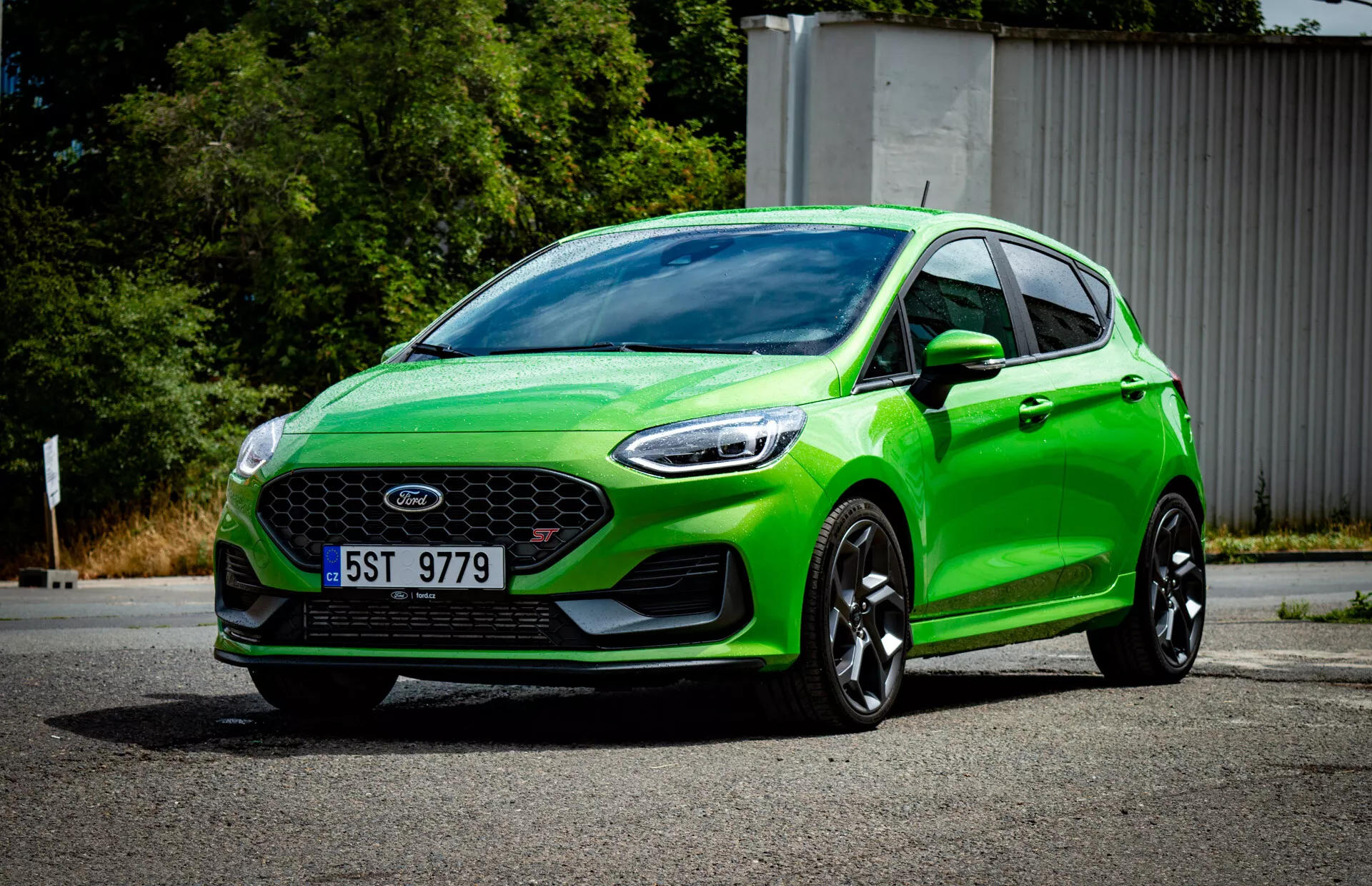 Živozelený hatchback Ford Fiesta 2022 v trojštvrťovom prednom pohľade ukazujúci prednú mriežku so znakom, športový nárazník s hmlovými svetlami, ostré uhlové svetlomety, aerodynamické kontúry, veľké čierne zliatinové kolesá a moderný systém osvetlenia