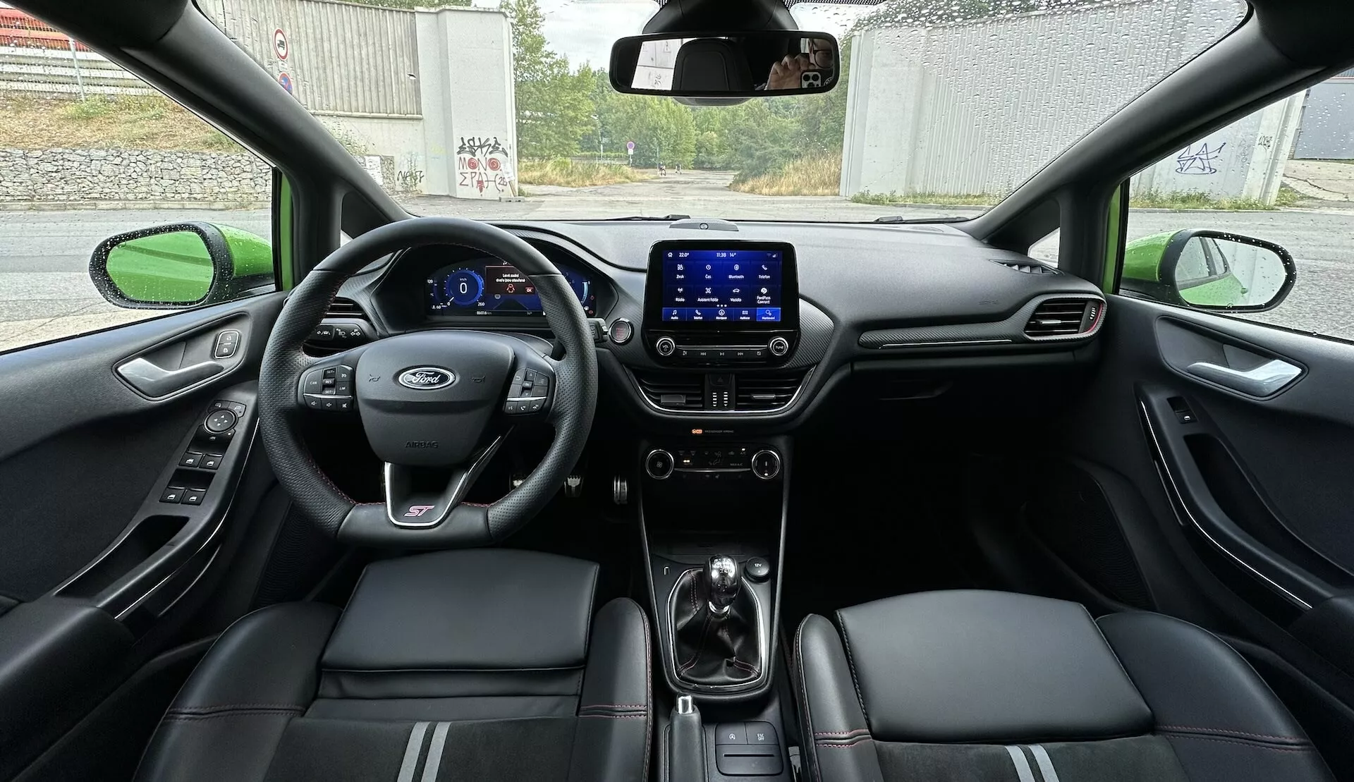Interiér Ford Fiesta 2022 z pohľadu zo zadného sedadla, ukazuje celý kokpit s digitálnym palubným doskou, multifunkčným volantom a koženými sedadlami so štepovanými akcentmi