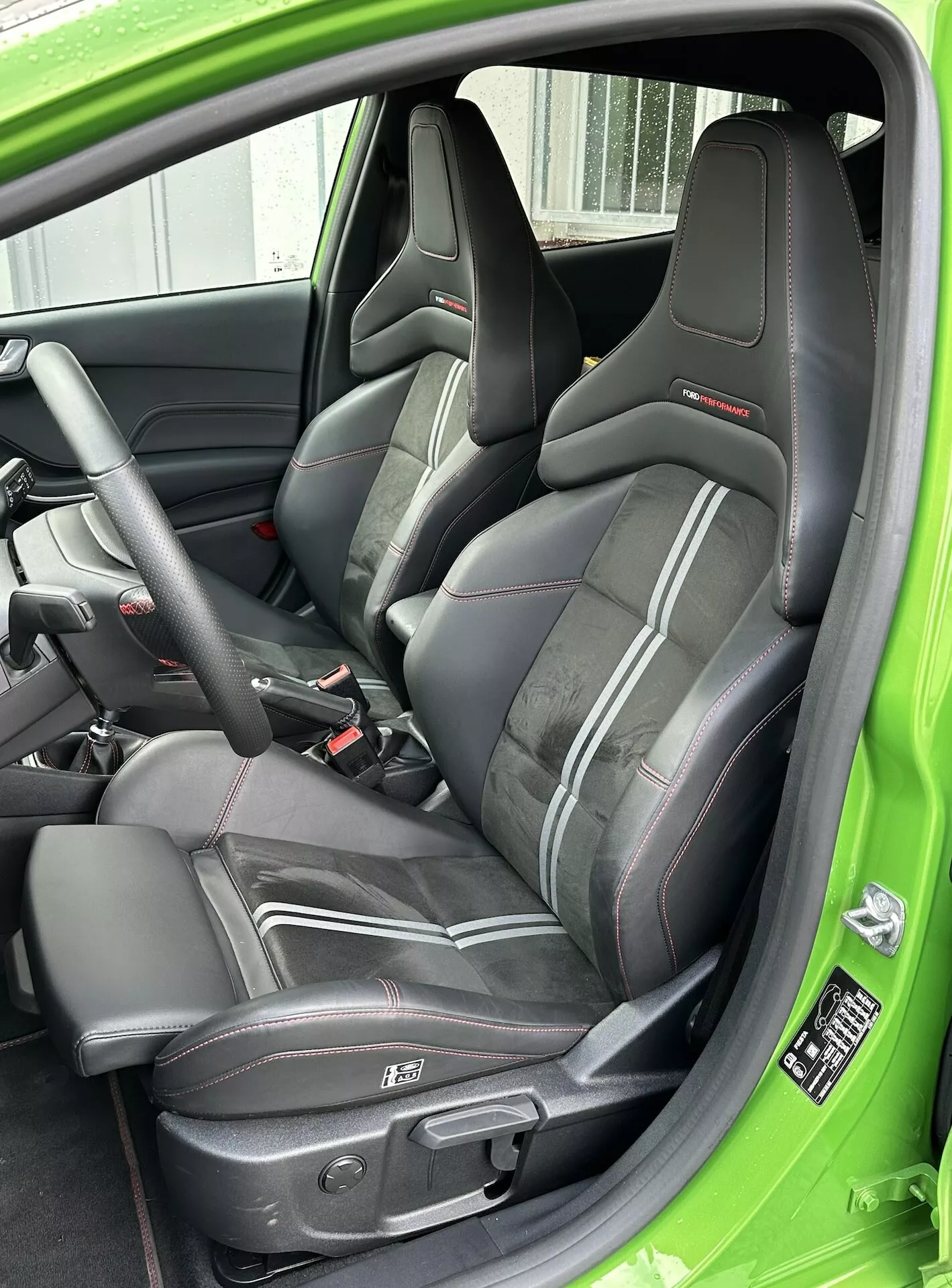 Detailný pohľad na športové kožené vodičské sedadlo s červenou lemovkou, trojbodový bezpečnostný pás a elektrické ovládanie sedadla, zdôraznený zelenou výzdobou interiéru Ford Fiesta 2022.