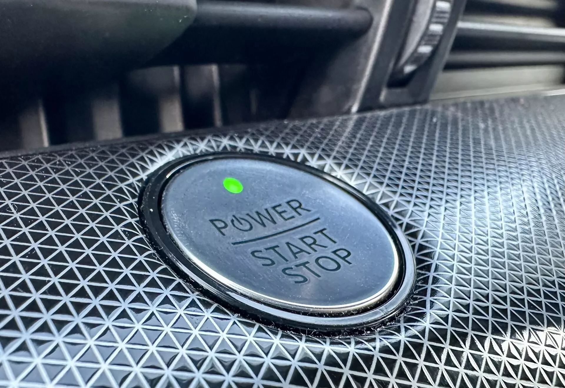 Detailný pohľad na tlačidlo pre štart/stop v aute Ford Mustang-Mach-E 2020, s textom 'POWER START STOP', zeleným indikátorom a textúrovaným okolitým dizajnom