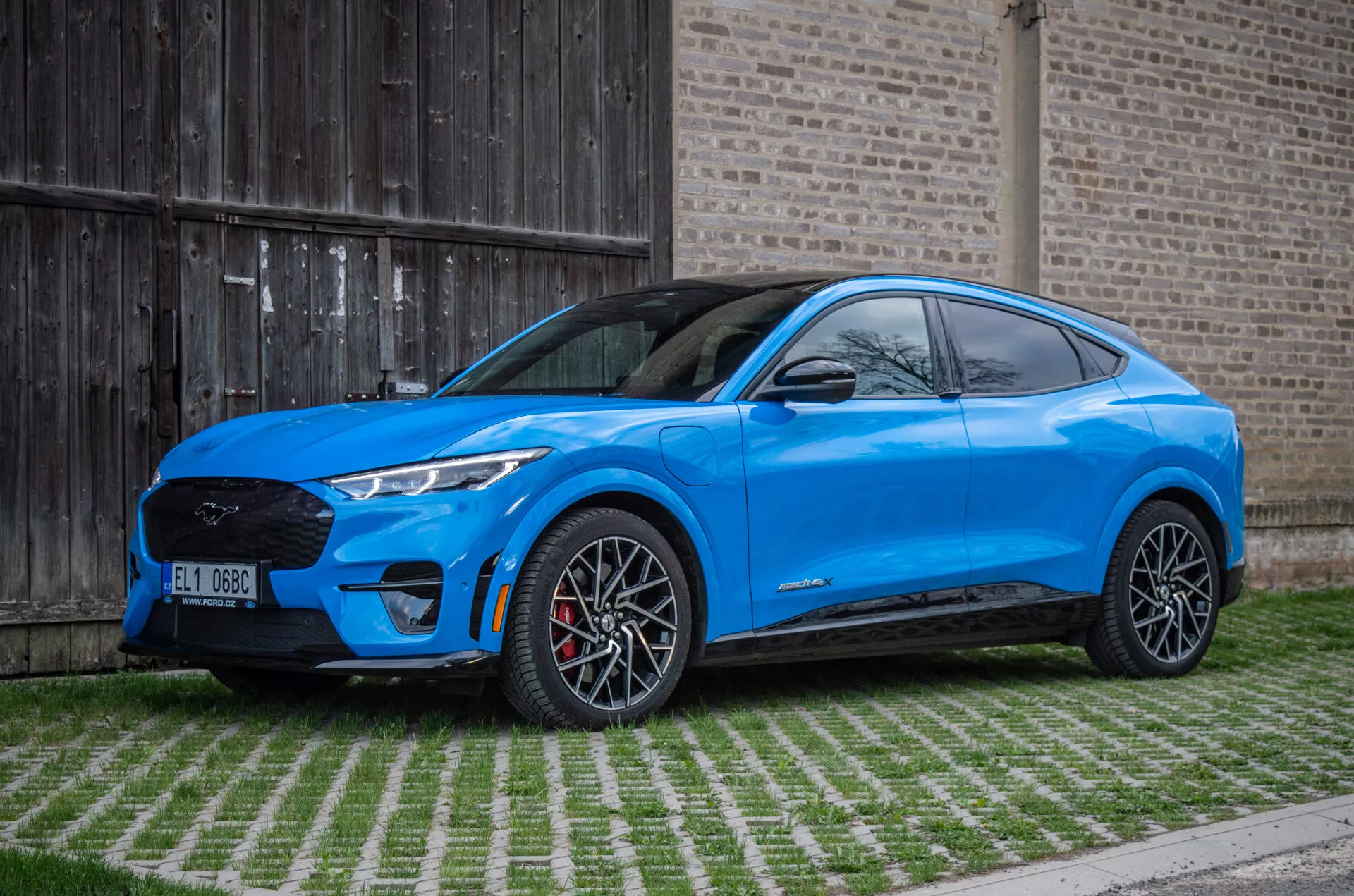 Ford Mustang Mach-E 2020 v jasne modrej farbe ukazuje bočný profil s veľkými zliatinovými kolesami, elegantnými LED svetlometmi a moderným dizajnom SUV na pozadí šetrnom k životnému prostrediu