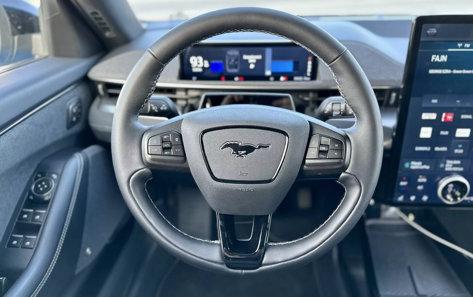 Interiér Ford Mustang-Mach-E 2020 z pohľadu vodiča, obsahujúci volant s troma ramenami s ovládacími prvkami, digitálny palubný počítač a veľký dotykový displej pre informačno-zábavný systém