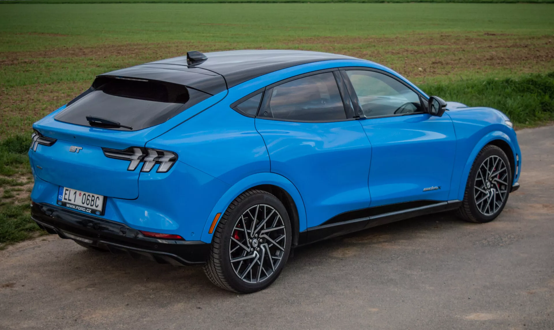 Svetlomodré elektrické SUV Ford Mustang Mach-E 2020 v dynamickom zobrazení zo zadnej strany pod uhlom troch štvrtín zdôrazňujúce aerodynamický dizajn, štýlové zadné svetlá a športové zliatinové kolesá, predvádzajúce pokročilú technológiu a elektrický pohon.