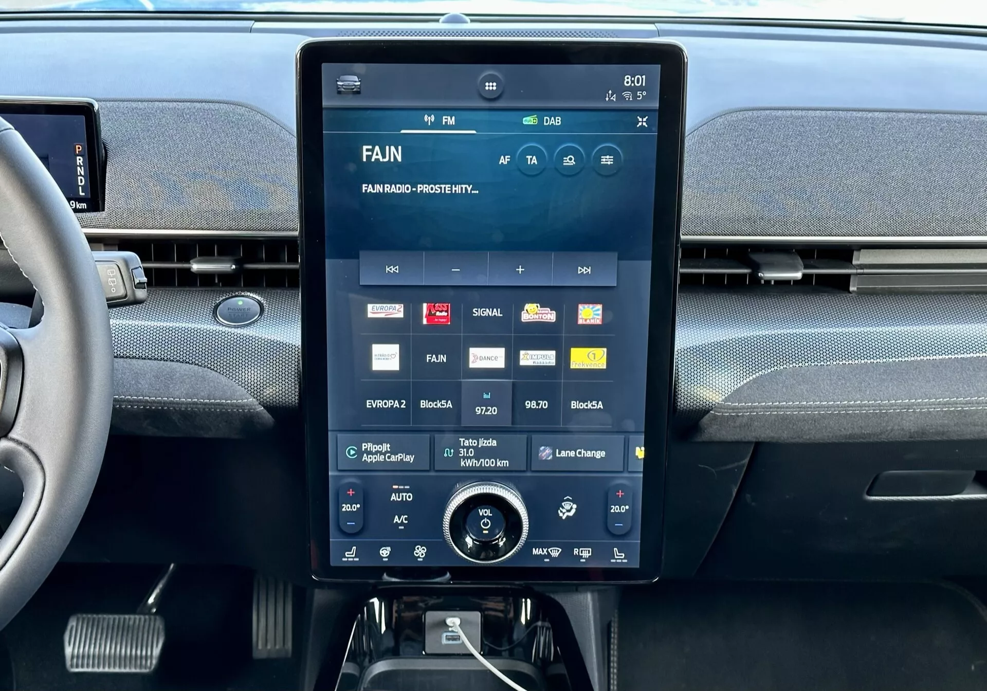 Interiérová centrálna konzola Ford Mustang Mach-E 2020 s veľkým dotykovým displejom zobrazujúcim multimediálne rozhranie s aplikáciami a nastaveniami, integrované vetracie otvory hore a ďalší otočný ovládač klímy dole.