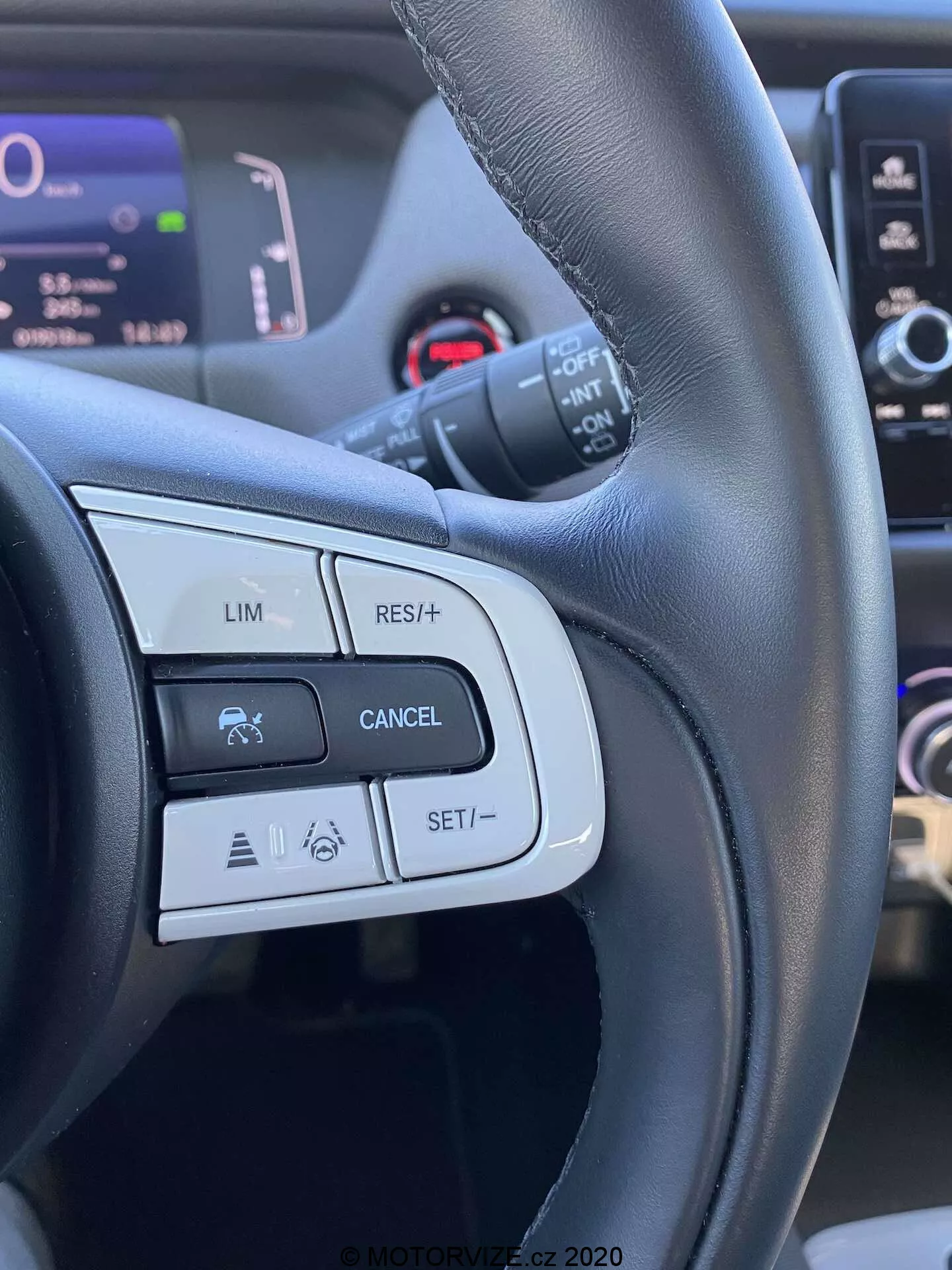 Podrobný pohľad na ovládacie prvky volantu Honda Jazz 2020 Crosstar, zameraný na tlačidlá a funkcie na ľavej strane ako LIM (obmedzovač rýchlosti), RES/+ (obnovenie alebo zvýšenie rýchlosti), CANCEL a SET/- (nastavenie alebo zníženie rýchlosti). Obrázok je urobený z pohľadu vodiča, zvýrazňuje čierny kožený volant s matovou a lesklou úpravou a zobrazuje ikony súvisiace s tempomatom a možnými pokročilými systémami asistencie vodiča.
