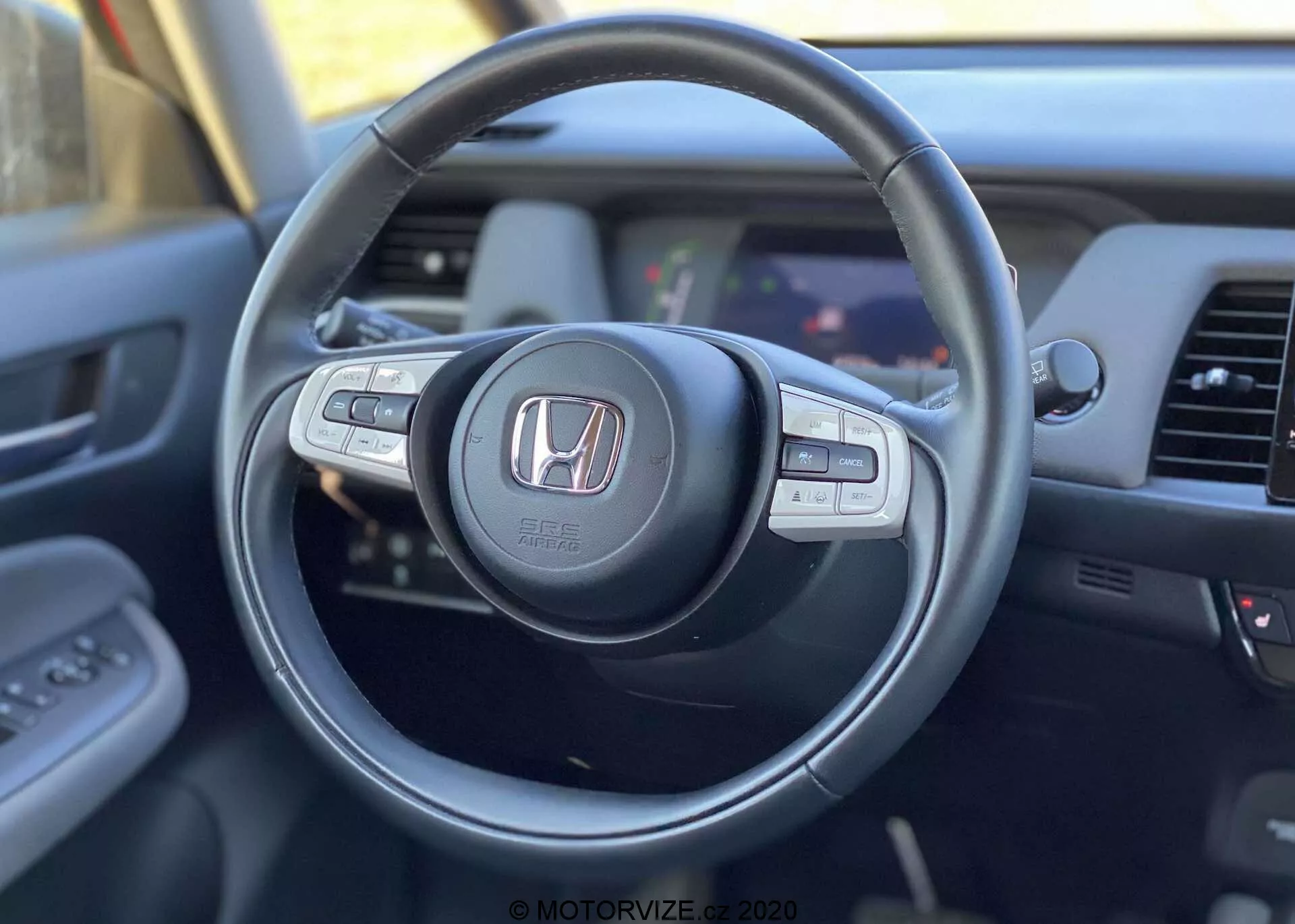 Výhľad na interiér Honda Jazz Crosstar 2020 z pohľadu vodiča, so zameraním na moderný volant s logom Honda, vybavený multifunkčnými ovládacími tlačidlami na audio, tempomat a handsfree volanie, s čiastočným pohľadom na palubnú dosku a informačný systém.