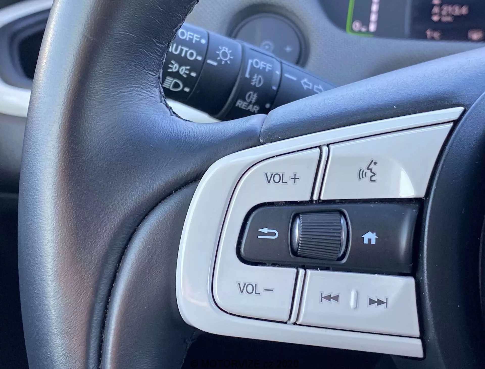 Detailný pohľad na ovládacie prvky na volante modelu Honda Jazz Crosstar 2020 ukazujúci nastavenie hlasitosti, hands-free telefónny systém a možné ovládanie tempomatu alebo výber skladieb. Stredný dôraz na kožený volant so strieborným lemovaním zdôrazňujúce pohodlie a elegantný dizajn.