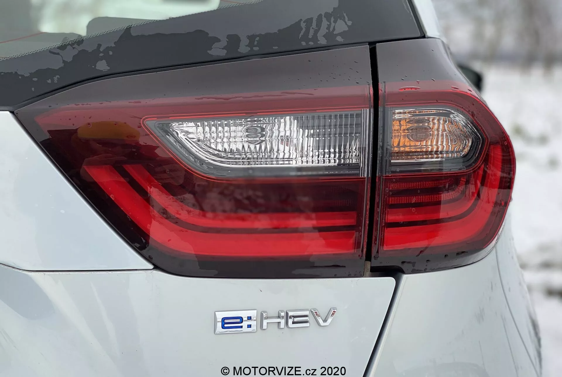 Honda Jazz 2020 Zadný Detailný Záber: S Hybridným Odznakom 'e:HEV' a Moderným LED Zadným Svetlom. Obrázok zvýrazňuje strieborno-šedú karosériu s prepracovaným dizajnom zadného svetla z nízkeho 45-stupňového uhla.