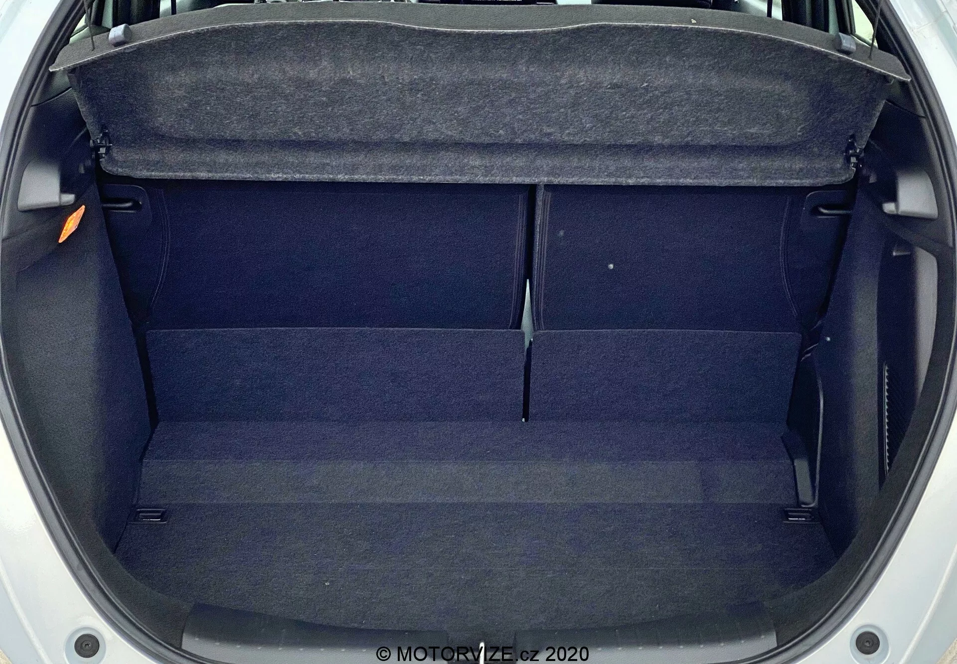 Pohľad zhora na prázdny kufor Honda Jazz 2020, ukazujúci stredne veľký, obdĺžnikový priestor s tmavou látkovou výplňou. Funkcie zahŕňajú balík policu hore, vnútorné lišty po stranách a mierne zvýšenie v strede. Kufor je čistý, neblokovaný a zdá sa dobre udržiavaný.