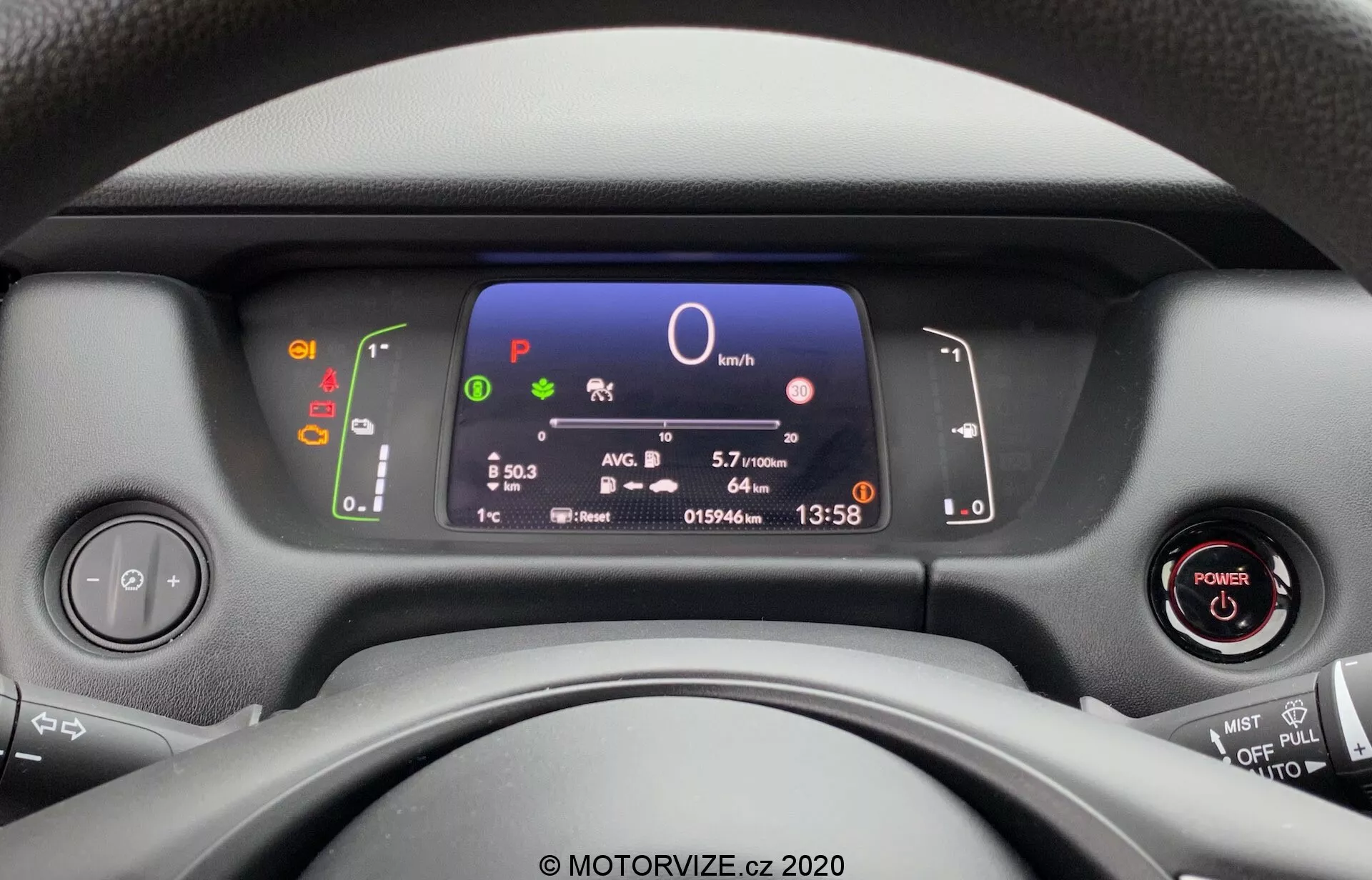 Pohľad zo sedadla vodiča na moderné prístrojové panely, volant a ovládacie prvky prístrojovej dosky v Honda Jazz 2020. Digitálny displej zobrazuje kľúčové informácie o vozidle vrátane rýchlosti, výberu prevodového stupňa, efektivity paliva, času a teploty, s viditeľným bezkľúčovým zapaľovaním a multifunkčnými ovládacími prvkami na volante.