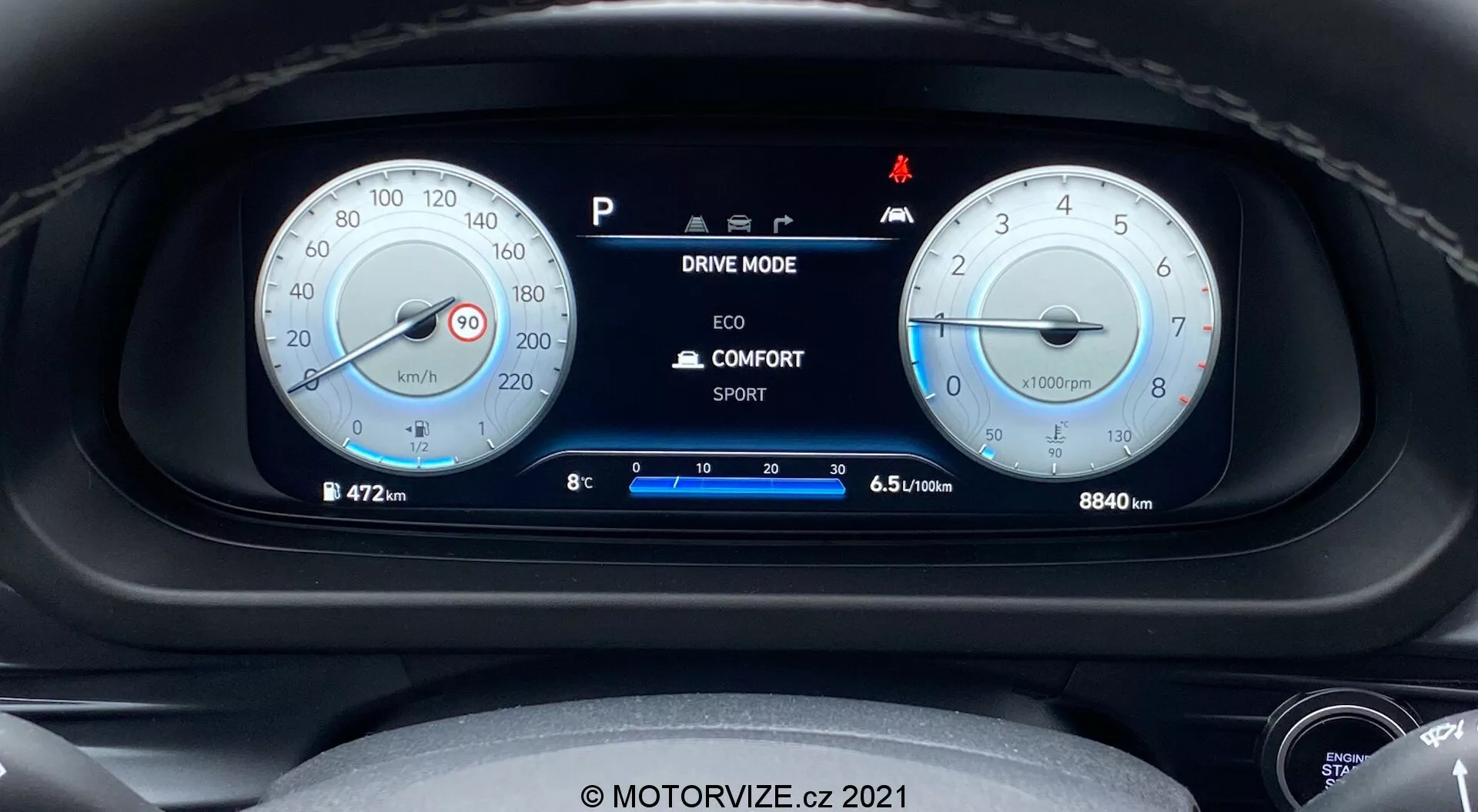 Detailný pohľad na prístrojovú dosku Hyundai i20 2020 z pohľadu vodiča, so dvoma hlavnými okrúhlymi analógovými ukazovateľmi a centrálnym digitálnym displejom. Ľavý ukazovateľ zobrazuje rýchlomer kalibrovaný do 260 km/h, zatiaľ čo pravý ukazovateľ je otáčkomer s červenou čiarou pri 6500 ot./min. Digitálny displej v strede zobrazuje možnosti jazdných režimov, vonkajšiu teplotu, polohu radenia a účinnosť paliva. Počítadlo kilometrov ukazuje 8840 km. Viditeľné sú rôzne kontrolky, vrátane jednej pre automatickú funkciu Štart/Stop. Obraz je ostrý a dobre osvetlený, s miernym zmäkčením okolo okrajov ukazovateľov. Obsahuje vodoznak 'MOTORVIZE.cz 2021'.