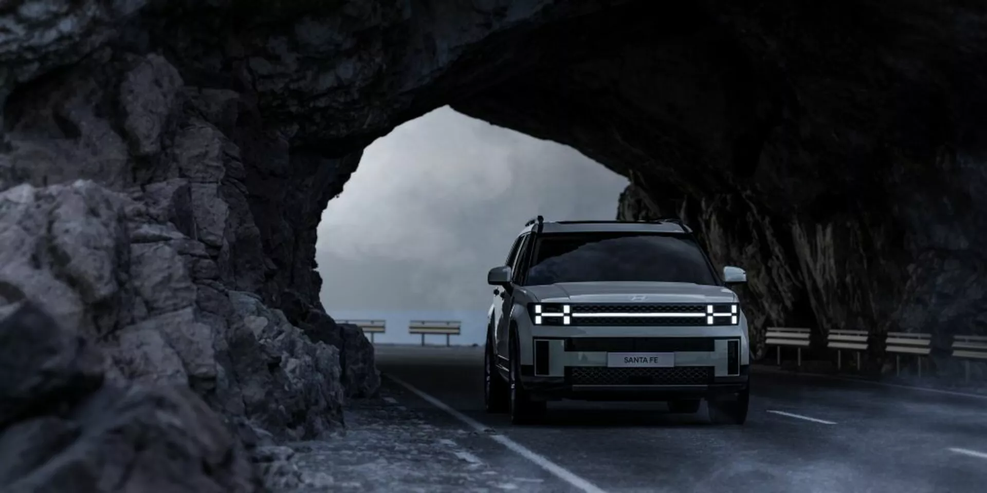 Predný pohľad na Hyundai Santa Fe 2024 (5. generácia) v skalnom tuneli, zvýrazňujúci horizontálne LED svetlá, veľkú prednú mriežku, čo naznačuje možný elektrický model, a luxusný dizajn s osvetleným logom, zachytený v jemnom osvetlení, zdôrazňujúci jeho robustný off-road potenciál.