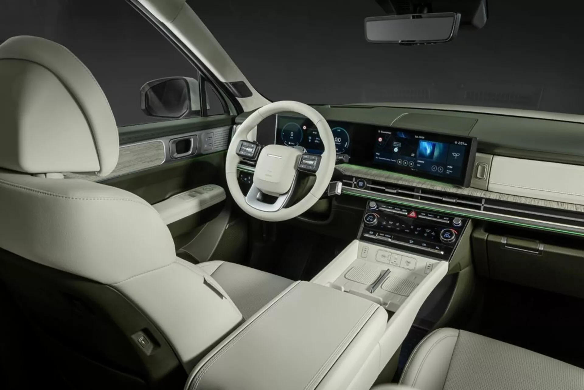 Pohľad do interiéru Hyundai Santa Fe 2024 (5. generácia) z rearnej pravej perspektívy, ukazujúci vodičovu stranu. Moderné usporiadanie palubnej dosky zahŕňa multifunkčný volant s dotykovými ovládacími prvkami. Stredová konzola integruje veľký horizontálny dotykový infotainment systém, pravdepodobne ponúkajúci navigáciu, médiá a nastavenia vozidla. Pod ním sa nachádzajú digitálne displeje a ovládače riadiace dvojzónový klimatizačný systém. Luxusný interiér má kožené čalúnenie, kontrastné šitie a elegantné dekoračné prvky, vyžarujúce prémiové remeselné spracovanie. Pohodlné a priestranné predné sedadlá s elektrickým nastavením zvýrazňujú dôraz na pohodlie cestujúcich a pokročilé automobilové technológie.