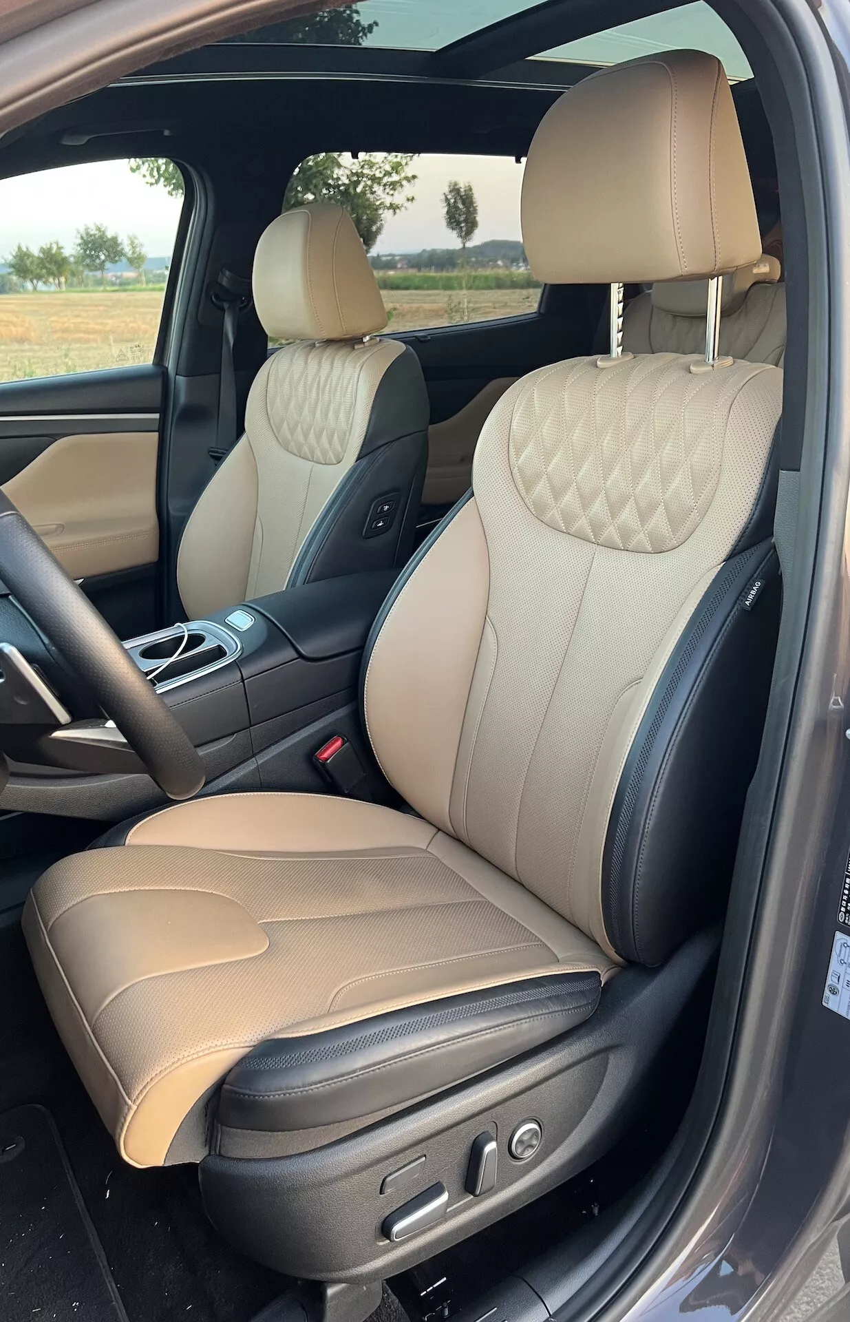 Interiérový pohľad na Hyundai Santa Fe 2020, so zameraním na luxusnú prednú pasažérsku oblasť s dvojfarebnými koženými sedadlami s diamantovým prešívaním, elektrickými ovládacími prvkami a sofistikovanými materiálmi, ako sú kartáčované kovové ozdoby a chrómované kľučky dverí.