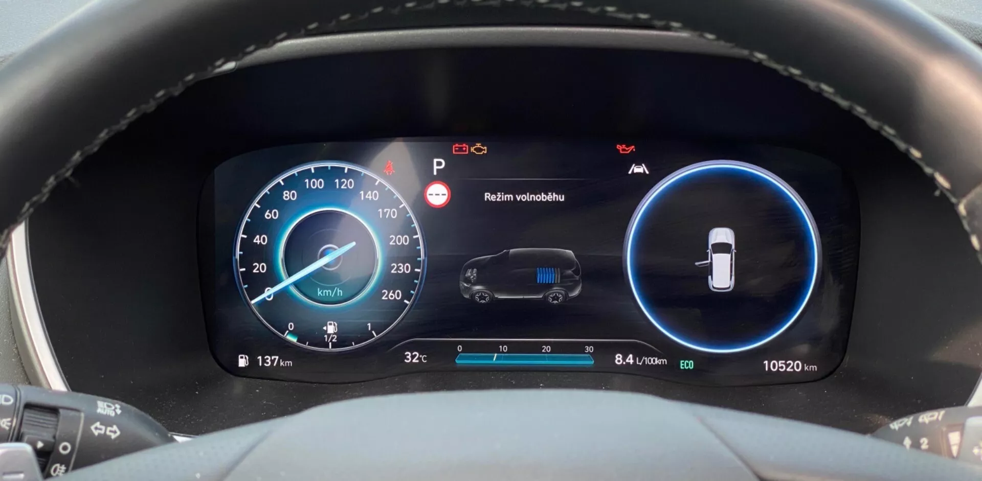 Detailný pohľad na moderný digitálny prístrojový panel v Hyundai Santa Fe 2020, ktorý je urobený z perspektívy vodiča. Zameriava sa na prístrojovú dosku a zobrazuje dva hlavné digitálne displeje v modrej a čiernej farbe. Ľavý displej zobrazuje rýchlomer s rýchlosťou 137 km/h a ďalšími indikátormi otáčok. Pravý displej monitoruje stav vozidla vrátane upozornenia na údržbu a varovania 'Zachovať viditeľnosť'. Dolná časť displejov zobrazuje vonkajšiu teplotu (3,2°C) a odometrovú hodnotu (10 520 km) spolu s efektivitou 8,4 litra na 100 kilometrov.