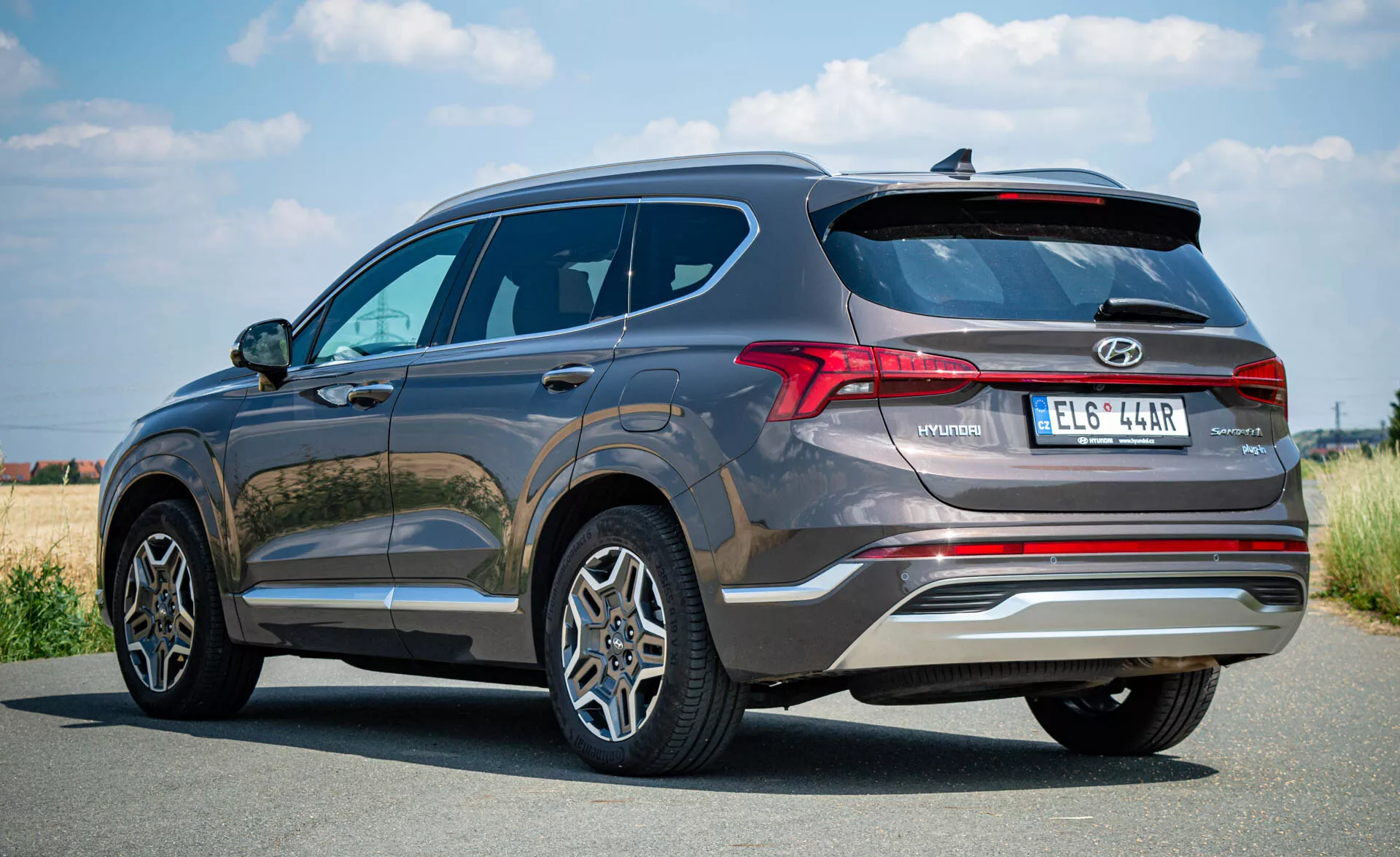 Zadopohľad na SUV Hyundai Santa-Fe 2020 ukazujúci jeho moderný dizajn, vrátane horizontálnych LED zadných svetiel, zliatinových kolies, dvojitých výfukových koncoviek a zadného nárazníka so senzormi. Viditeľné črty zahŕňajú zatmavené okná a odznaky modelov, všetko zachytené na ničím nerušenej asfaltovej ceste.
