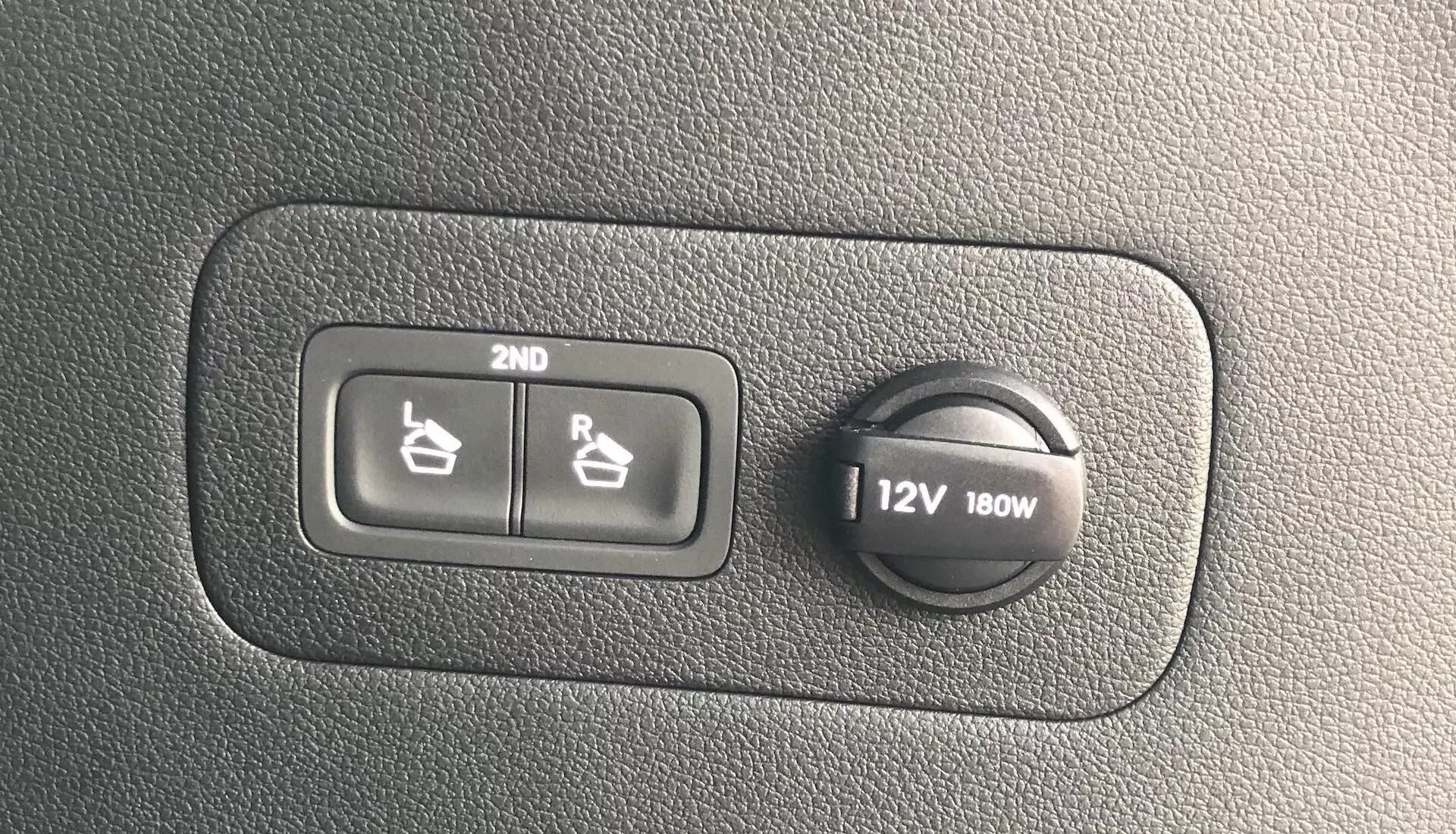 Detail interiéru Hyundai Santa Fe 2020 zobrazujúci ovládanie vyhrievania sedadiel pre druhý rad a 12V zásuvku 180W na textúrovanom plastovom povrchu.