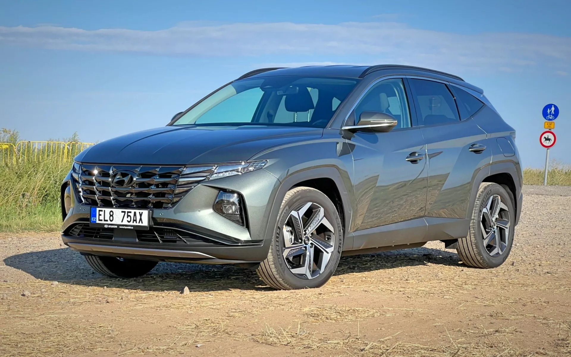 Moderné SUV Hyundai Tucson 2020 zobrazené z trojštvrtečného predného uhla, predvádzajúce jeho výraznú mriežku, elegantné svetlomety, prednú časť, sochársky tvarovanú kapotu a zliatinové kolesá na nespevnenej odstavnej ploche pod jasnou oblohou