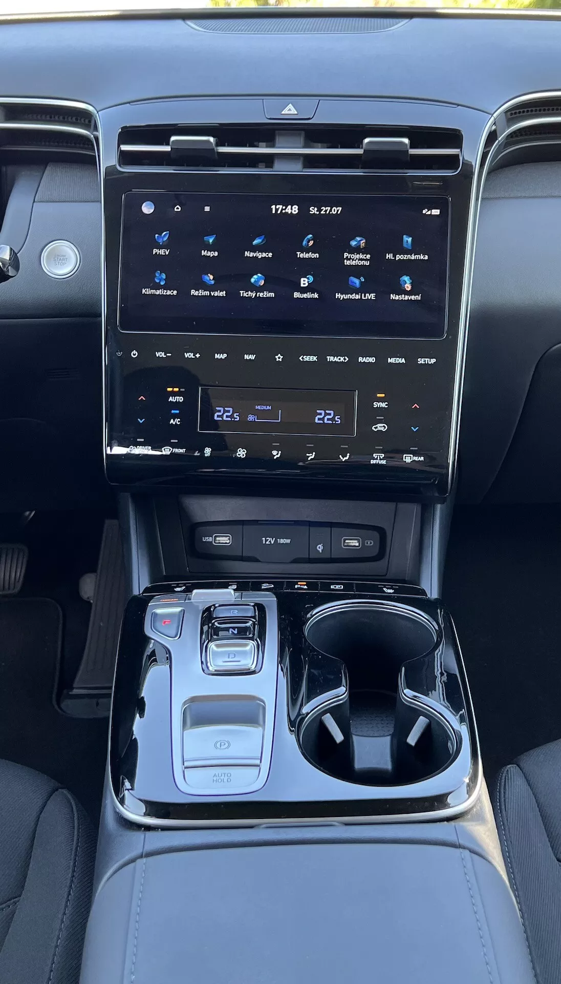 Interiér Hyundai Tucson 2020 ukazujúci stredovú konzolu s veľkým dotykovým informačným systémom, tlačidlami na ovládanie klímy, elektronickým výberom prevodov, tlačidlom na výber jazdného režimu, držiakmi na nápoje, úložným priestorom a ambientným osvetlením.