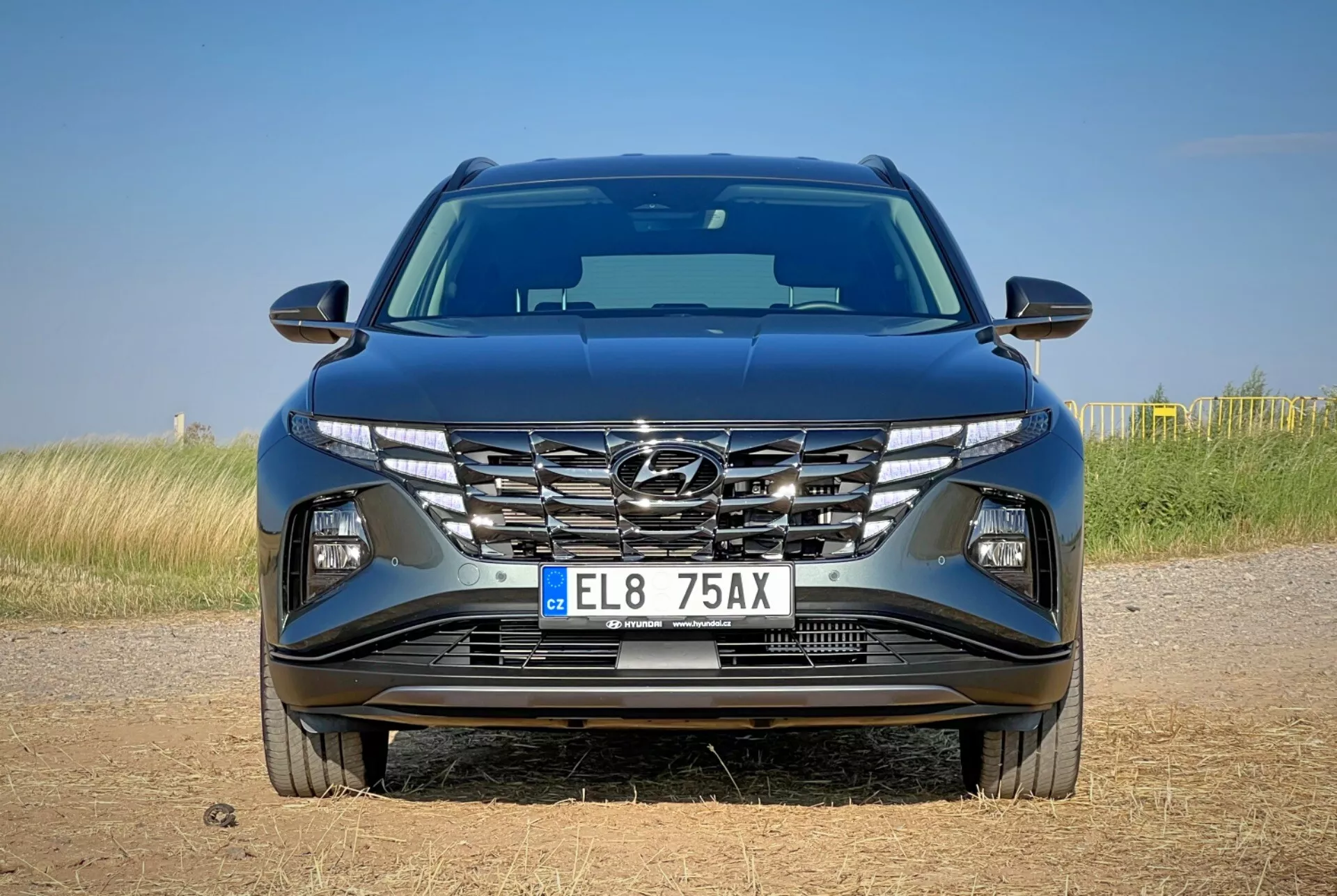 Predný pohľad na Hyundai Tucson 2020 ukazujúci aerodynamický dizajn kapoty, kaskádovú mriežku, ostré LED svetlomety a detailný nárazník s možnými technologickými funkciami, umiestnený na pozadí prírodnej krajiny
