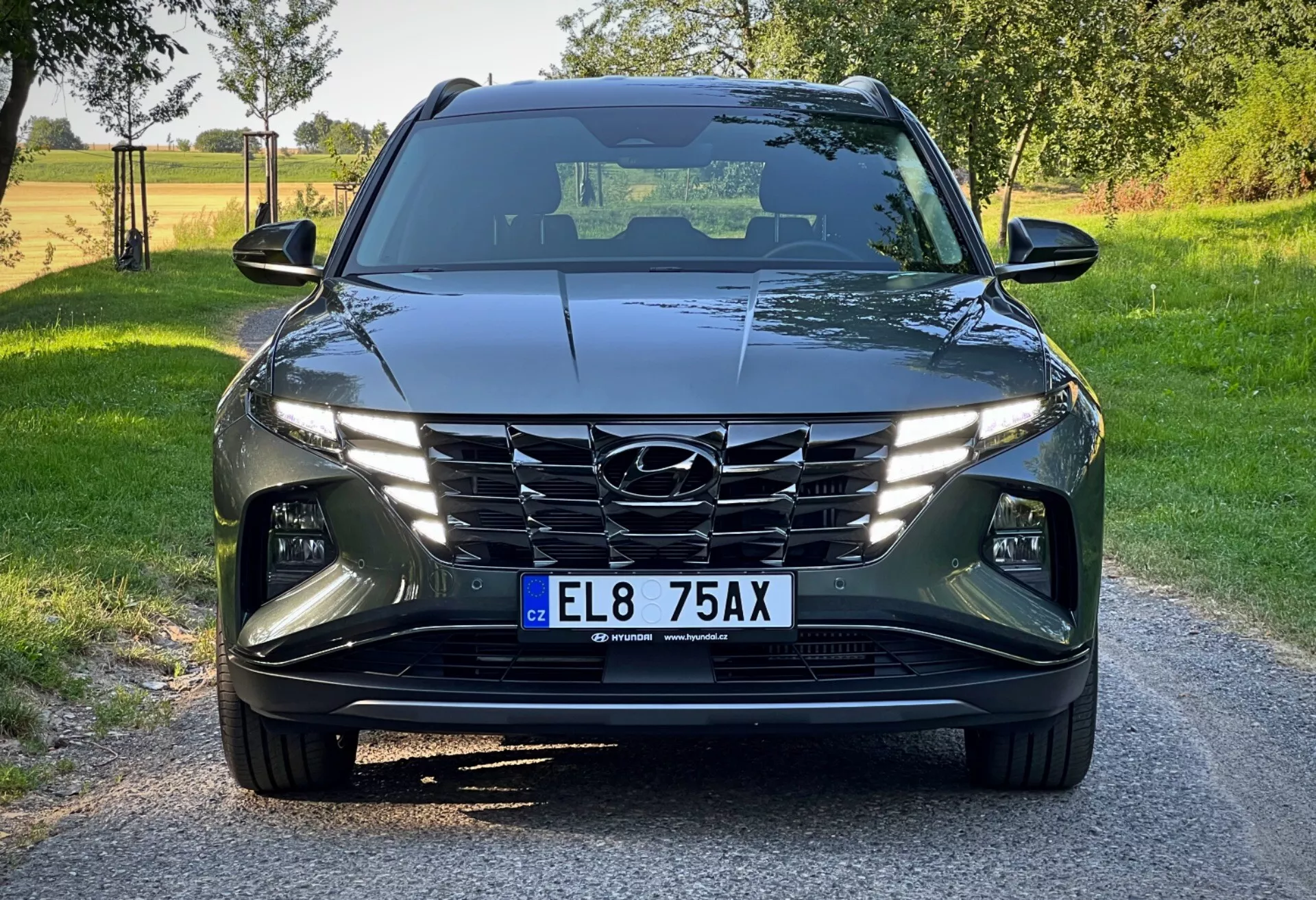 Hyundai Tucson 2020 zobrazený z prednej perspektívy pod nízkym uhlom, predvádzajúci jeho moderný dizajn s prudkými, uhlovými líniami, LED svetlometmi, kaskádovou mriežkou a pokročilými asistenčnými systémami vodiča na pozadí jasného vidieckeho dňa
