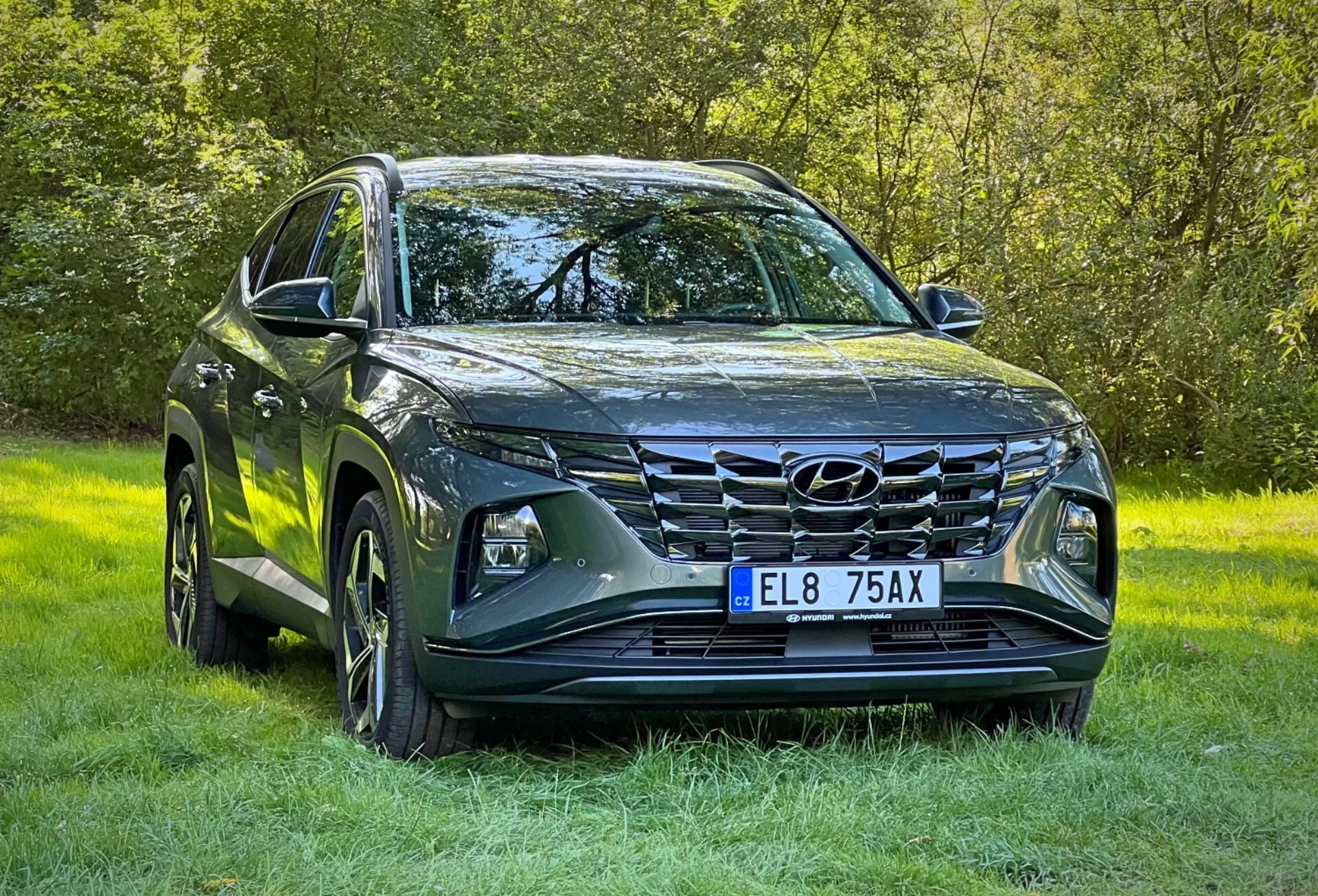 SUV Hyundai Tucson 2020 s metalickým povrchom, zobrazujúce LED svetlomety, výraznú prednú mriežku, sochársky navrhnutú kapotu, zliatinové kolesá a bočné zrkadlá s integrovanými smerovými signálmi, zaparkované na tráve zdôrazňujúce schopnosť jazdy v teréne