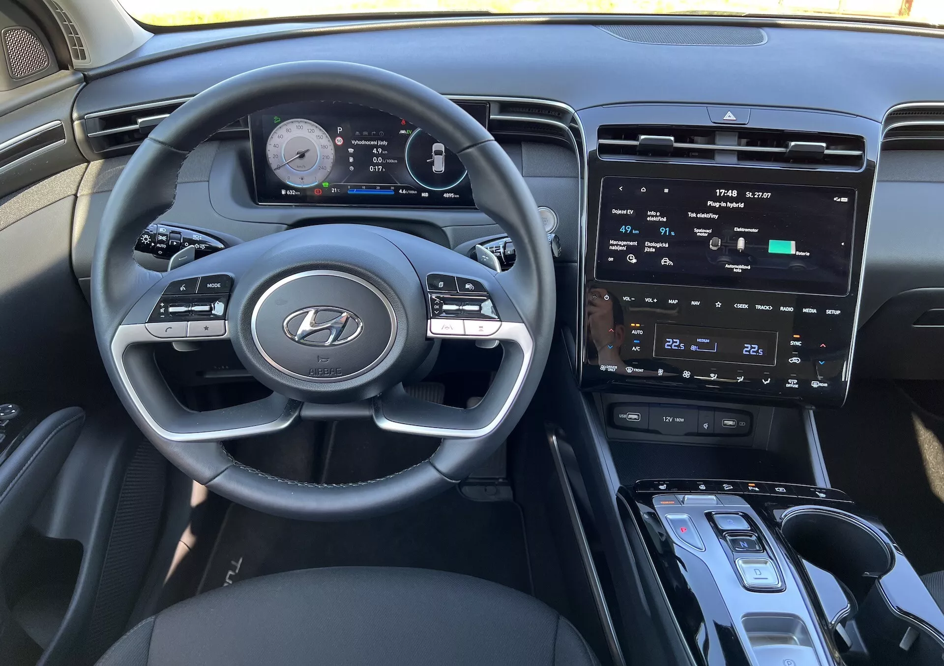 Interiér Hyundai Tucson 2020 s volantom s logom Hyundai, pokročilým digitálnym prístrojovým panelom, centrálnym dotykovým obrazovkou, ovládaním klimatizácie, tlačidlom štart/stop pre zapínanie, pákou prevodovky a možnou oblasťou pre bezdrôtové nabíjanie z pohľadu vodiča