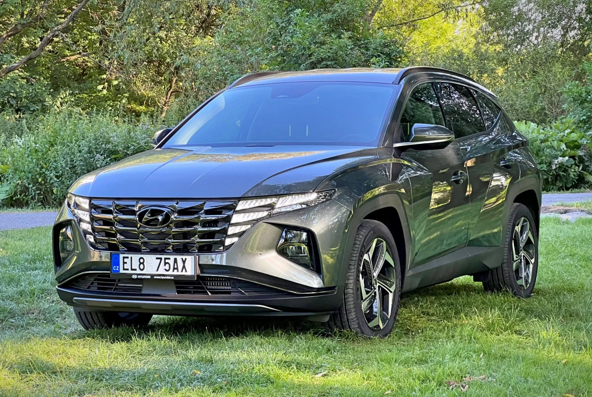 SUV Hyundai Tucson 2020 zaparkované na trávniku so stromami na pozadí, zobrazuje prednú mriežku, LED svetlomety a zliatinové kolesá