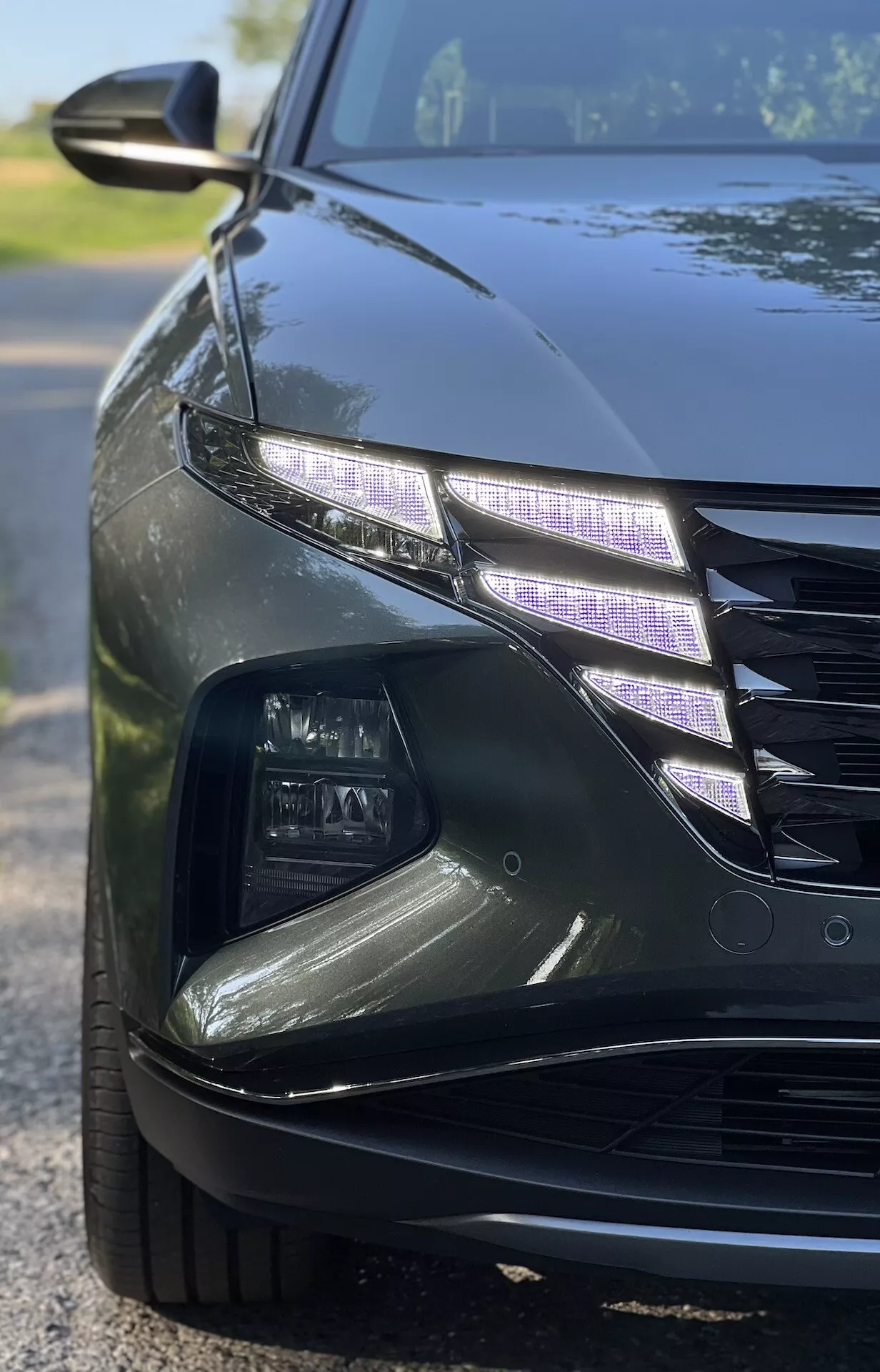 Zblízka uhlový pohľad na Hyundai Tucson 2020 ukazujúci zložitý dizajn LED svetlometov a časť mriežky s lesklým povrchom za slabého osvetlenia, ilustrujúci funkcie luxusného automobilu a modernú technológiu automobilového osvetlenia.
