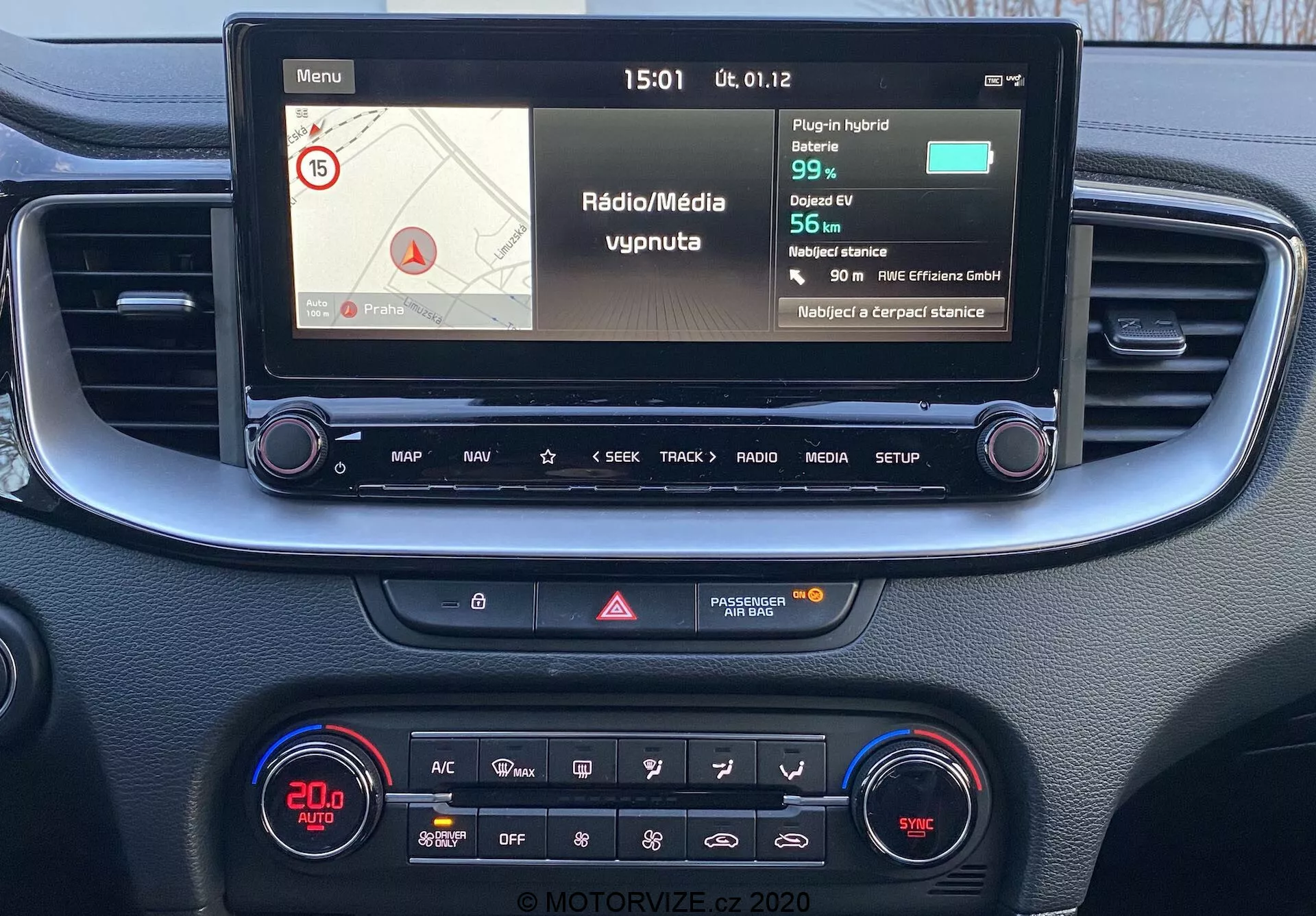 Pohľad z prvej osoby na stredovú konzolu a infotainment systém Kia Ceed 2018, s farebným displejom zobrazujúcim navigáciu a média, fyzickými tlačidlami na ovládanie a klimatizačným panelom s digitálnym displejom a rôznymi funkciami.