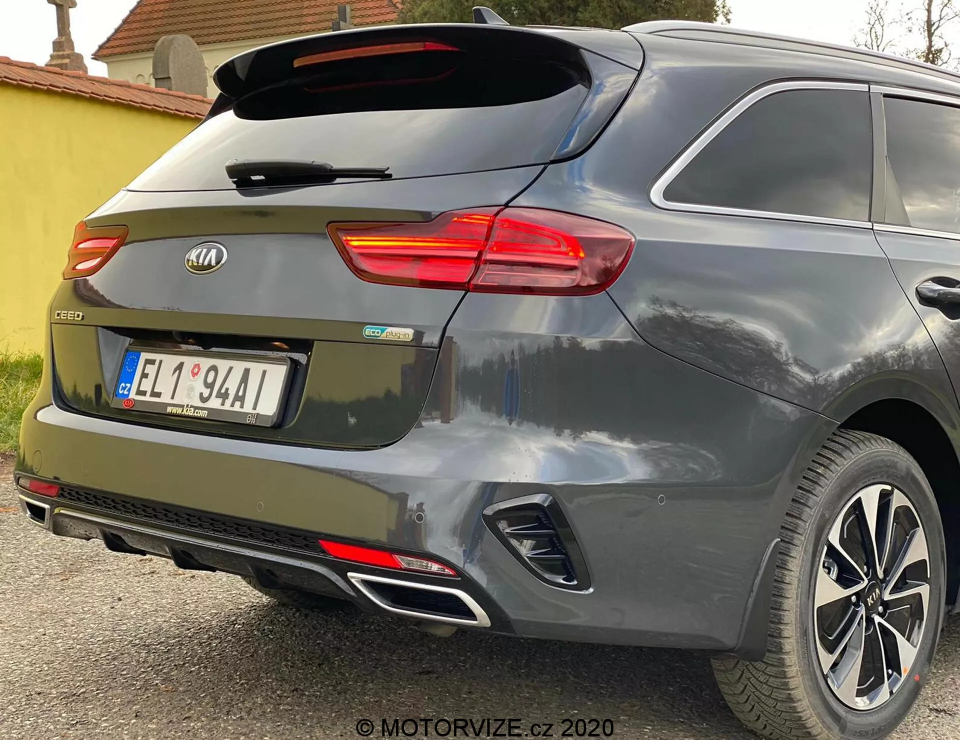 Čiastočný zadný uhol pohľadu na Kia Ceed 2018, zdôrazňujúci osvetlené pravé zadné svetlo, zadné čelné sklo so stierateľom, zadné dvere so značkovým emblémom a modelovým odznakom 'CEED', integrované reflektory v zadnom nárazníku, parkovacie senzory, dvojitý výfukový systém a zliatinové kolesá proti metalickej sivej alebo striebornej farbe.