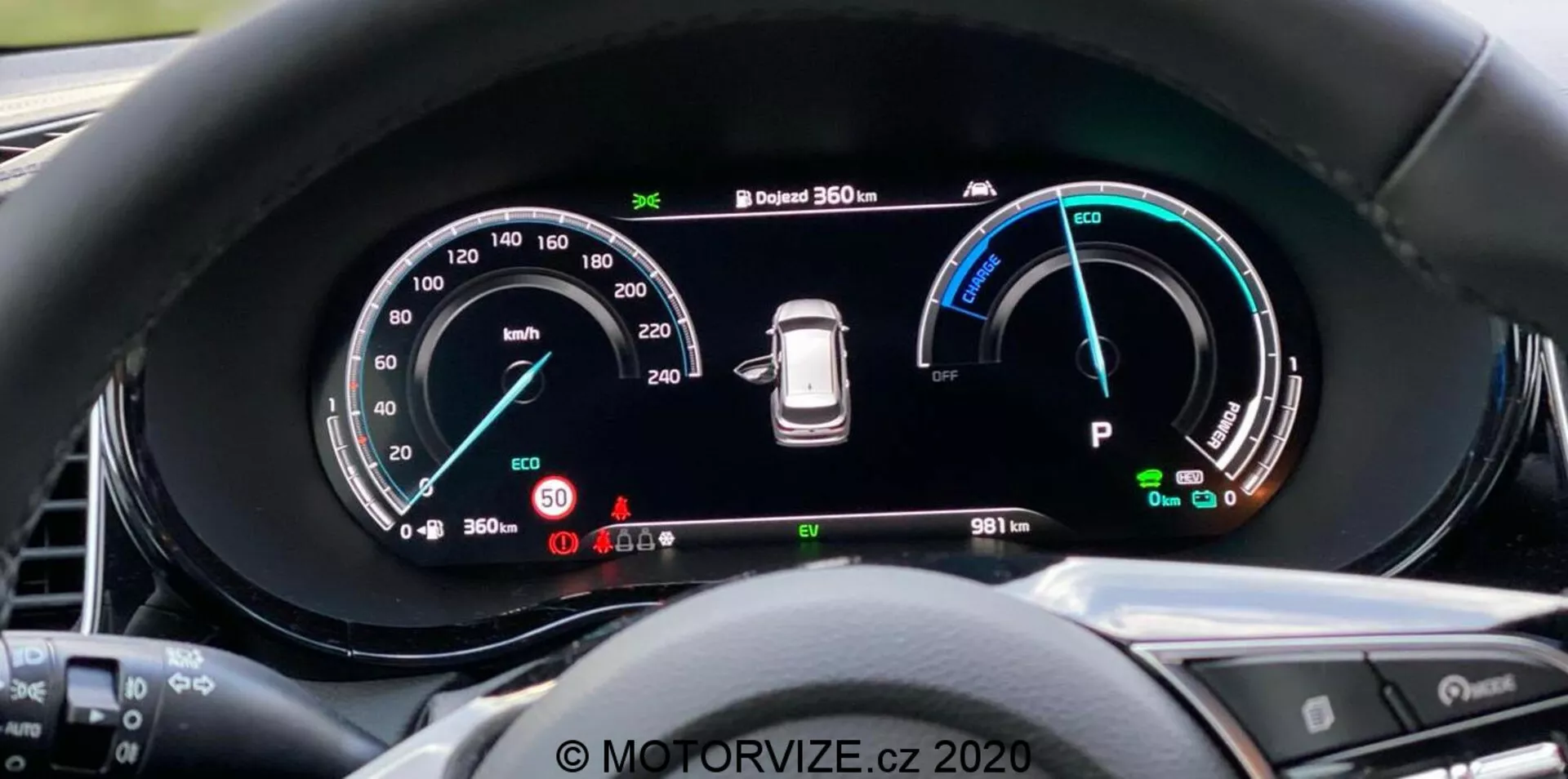 Detailný pohľad na digitálnu prístrojovú dosku Kia Ceed 2018 z pohľadu vodiča, s veľkým širokouhlým displejom s detailnými prístrojmi, vrátane rýchlomeru do 260 km/h, indikátora výkonu s režimami Eco, Comfort a Power, varovania tlaku v pneumatikách a indikátora režimu 'Park'. Prístrojová doska tiež ukazuje 360-stupňový kamerový systém a počítadlo kilometrov s hodnotou 9811 km. Okraj zabraňujúci oslneniu a čiastočne viditeľné tlačidlá volantu. Vodoznak 'MOTORVIZE.cz 2020'.