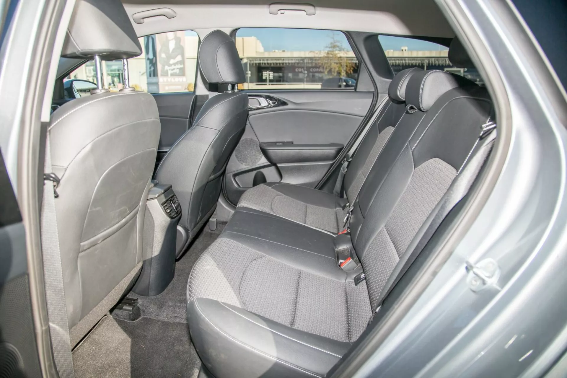 Vnútorný pohľad na Kia Cee'd 2009 predstavuje design a funkcie zadnej časti sedadla, zdôrazňuje odolnú dvojfarebnú tkaninovú čalúnenie, viditeľné bezpečnostné pásy, nastaviteľné opierky hlavy, dverový panel s úložným priestorom, potenciálne kotvy pre detské sedačky, kobercovú podlahu a ambientné osvetlenie klenby z pohľadu pravých zadných dverí.