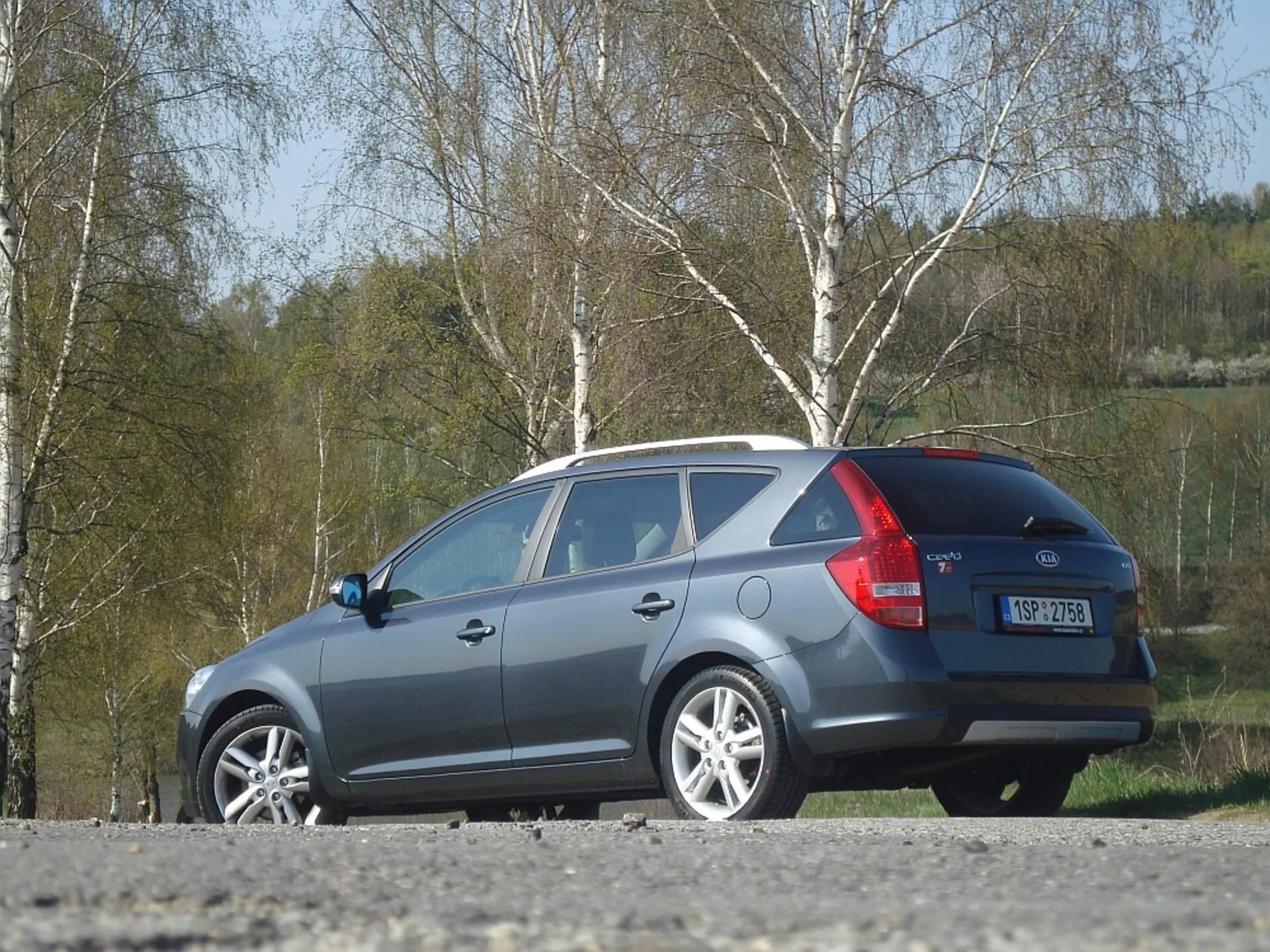 Šedé kombi Kia Ceed z roku 2009, zobrazujúce bok a zadnú časť s dôrazom na aerodynamický tvar strechy, zadné svetlá a zadné okno, zaparkované vonku
