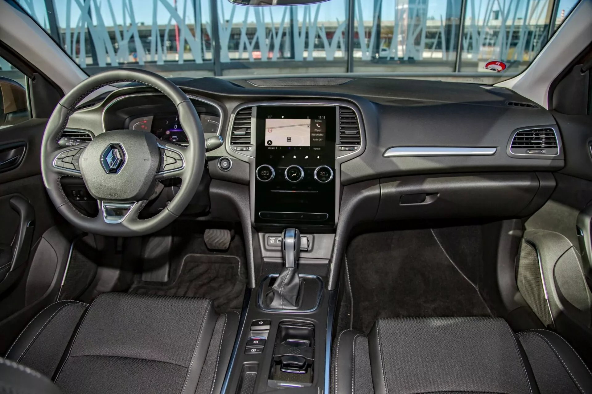 Interiér Kia Cee'd 2009 z pohľadu zadného sedadla ukazujúci multifunkčný volant, dotykový informačný systém, automatickú prevodovku a detailné čalúnenie v prednej časti kokpitu