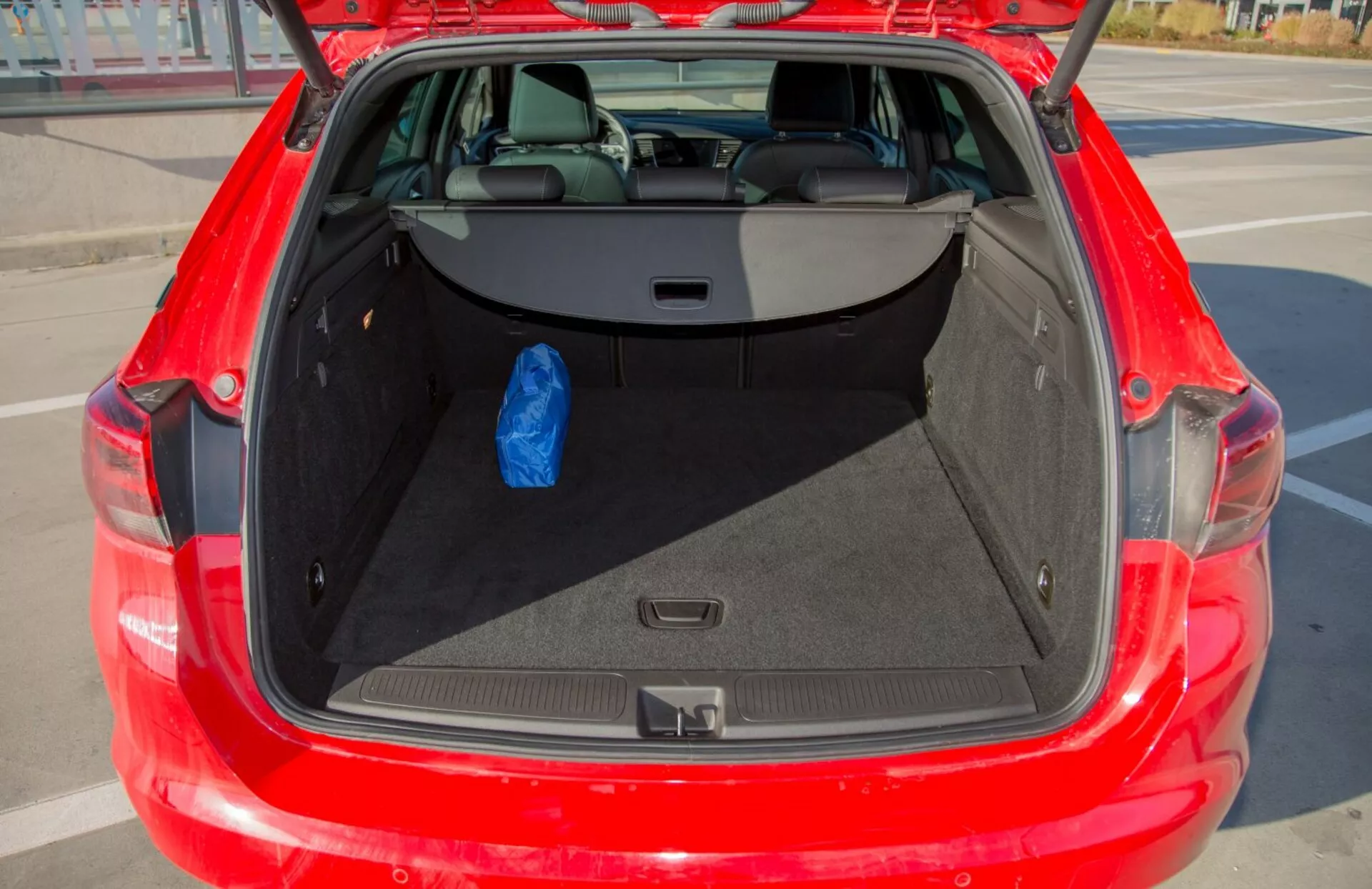 Detailný pohľad na otvorený kufor červeného Kia Cee'd z roku 2009, ukazujúci priestranný úložný priestor a zadné sedadlá delené v pomere 60/40, s jednou modrou taškou demonštrujúcou použiteľnosť.