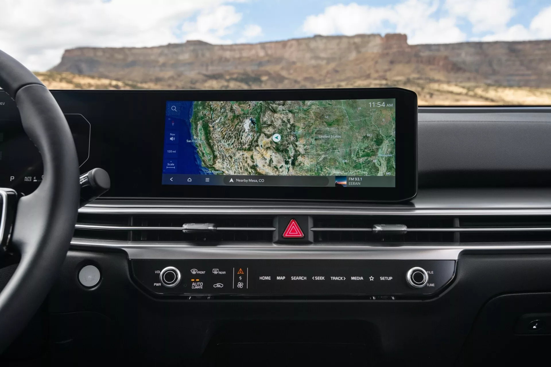 Interiér palubnej dosky Kia Sorento MQ4 facelift 2024 s širokým dotykovým displejom infotainmentu s GPS navigáciou, manuálnymi a dotykovými ovládaniami pre klimatizáciu a zvuk, tlačidlom výstražných svetiel a minimalistickým dizajnom s integrovanými vetracími otvormi, viditeľný z perspektívy vodiča