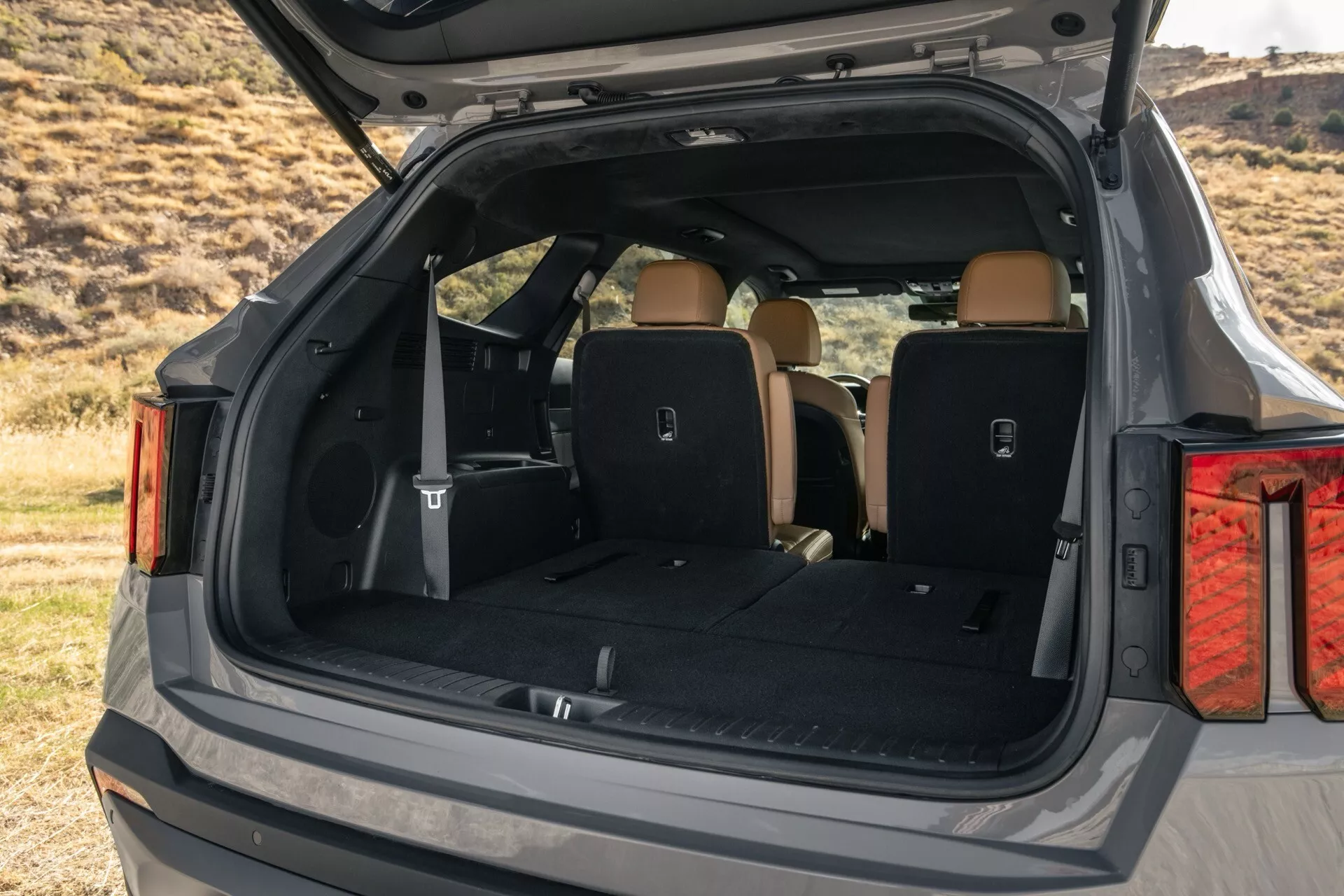Detailný pohľad na zadný nákladový priestor SUV Kia Sorento 2024 (MQ4-Facelift) s otvoreným kufrom, zobrazujúci rozšírený úložný priestor, svetlo béžový interiér, úchytky na náklad, elektrickú zásuvku a integrované krídlo, pohľad z pravého zadného uhla
