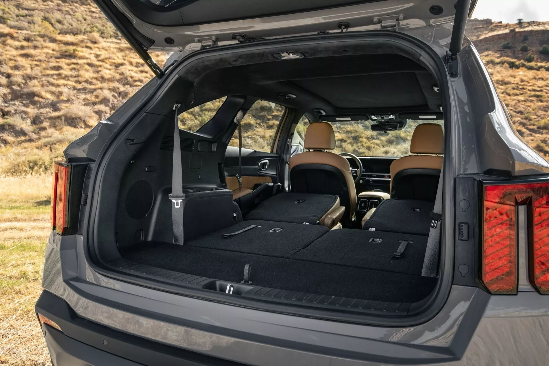 Facelift Kia Sorento MQ4 2024 ukazujúci priestranný nákladný priestor z šikmého zadného uhla, zdôrazňujúci vnútorný luxus a užitočné funkcie s tmavým exteriérom a svetlým interiérom