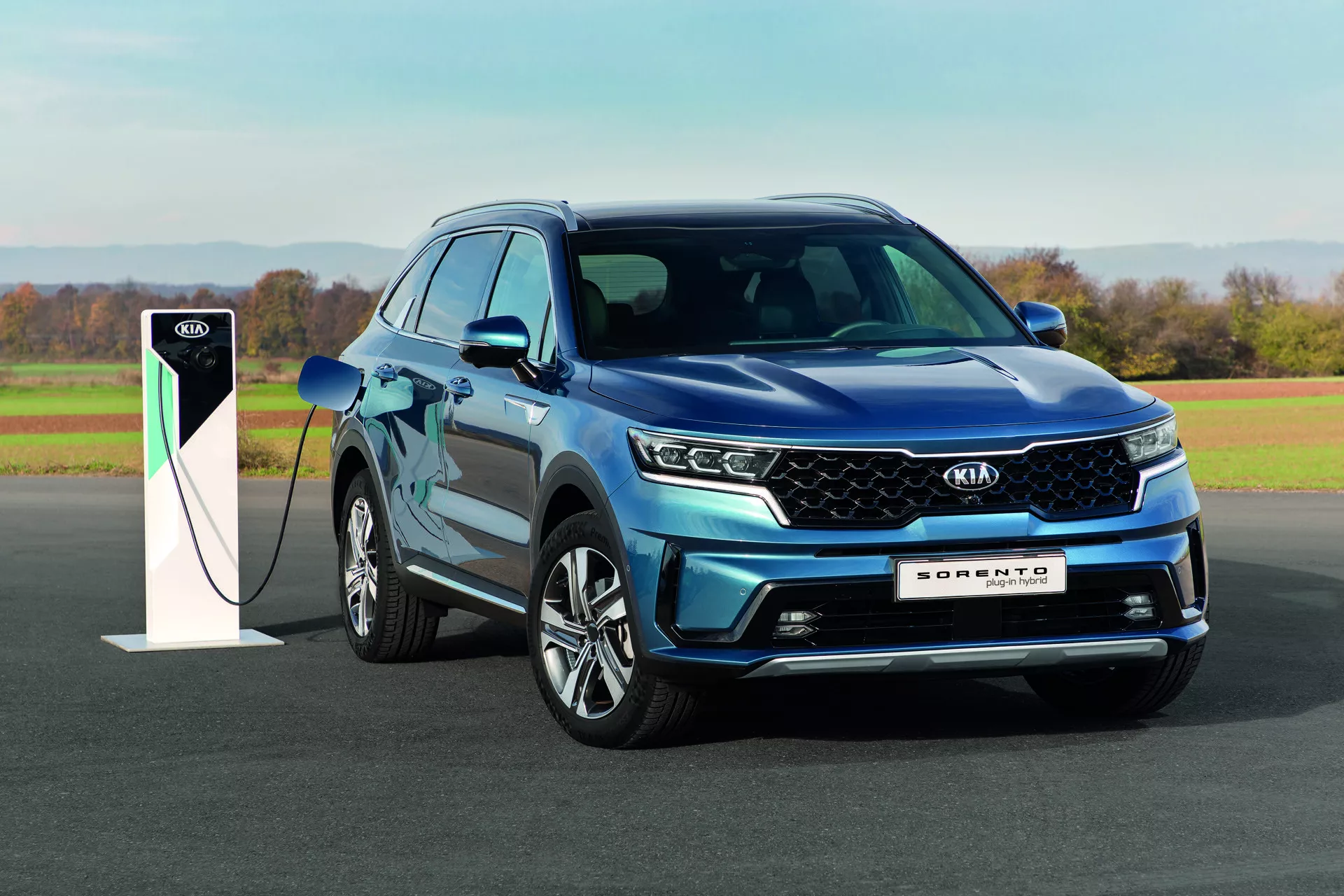 Modré SUV Kia Sorento 2020 s LED svetlometmi a technológiou plug-in hybrid, zaparkované vonku pri nabíjacej stanici na dennom svetle, ukazujúce dizajn a ekologické vlastnosti