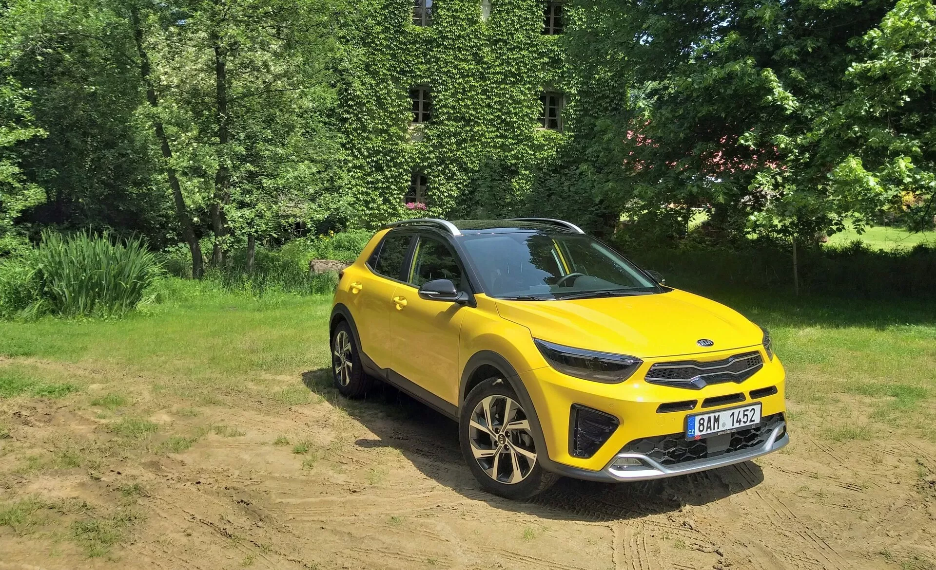 Žiarivo žlté crossover SUV Kia Stonic 2017 v trojštvrťovom prednom pohľade zvýrazňujúcom jeho prednú mriežku, LED svetlomety, kapotu a stranu vodiča, nastavené proti prírodnému pozadiu so slnečným svetlom na čistom pozemku, predvádzajúce schopnosti na ľahké off-road jazdenie, športové zliatinové kolesá a moderné dizajnové prvky.
