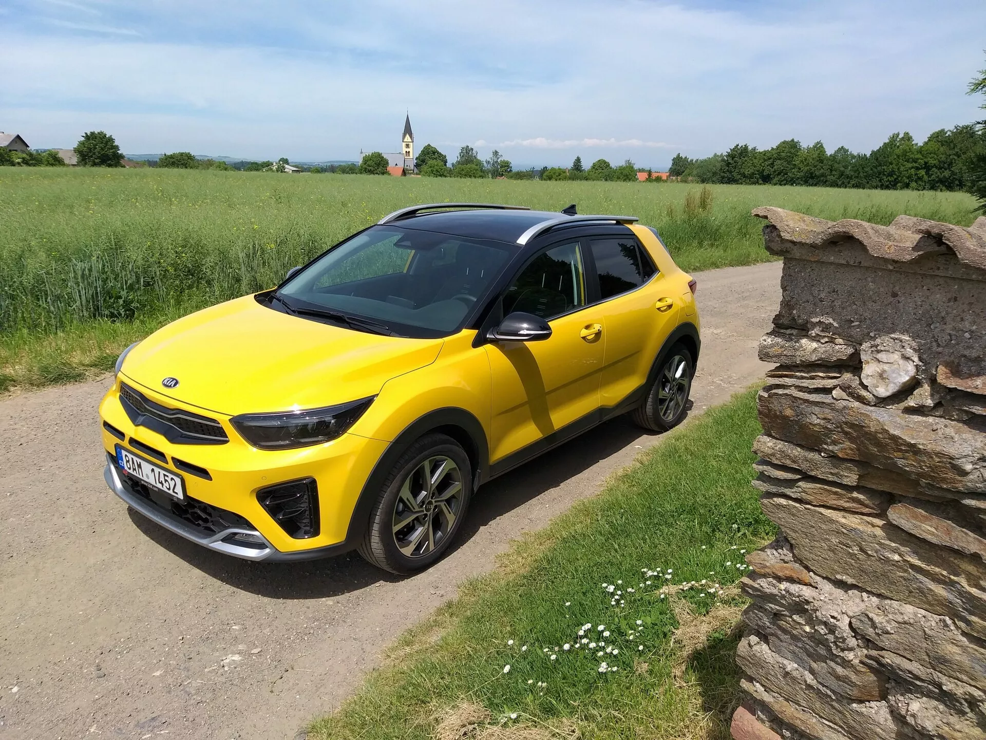 Svetložltý kompaktný SUV Kia Stonic 2017 s čiernou strechou, ktorý prezentuje svoj elegantný dizajn a dynamické kontúry z uhla tri štvrtiny na vidieckej prašnej ceste