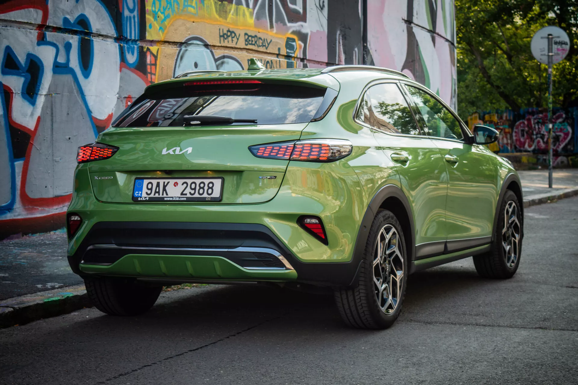 Kia XCeed 2022 vo výraznej zelenej farbe ukazuje svoj zadný trojštvrtečný uhol s európskou špz, LED zadnými svetlami, zliatinovými kolesami a mestským pozadím.