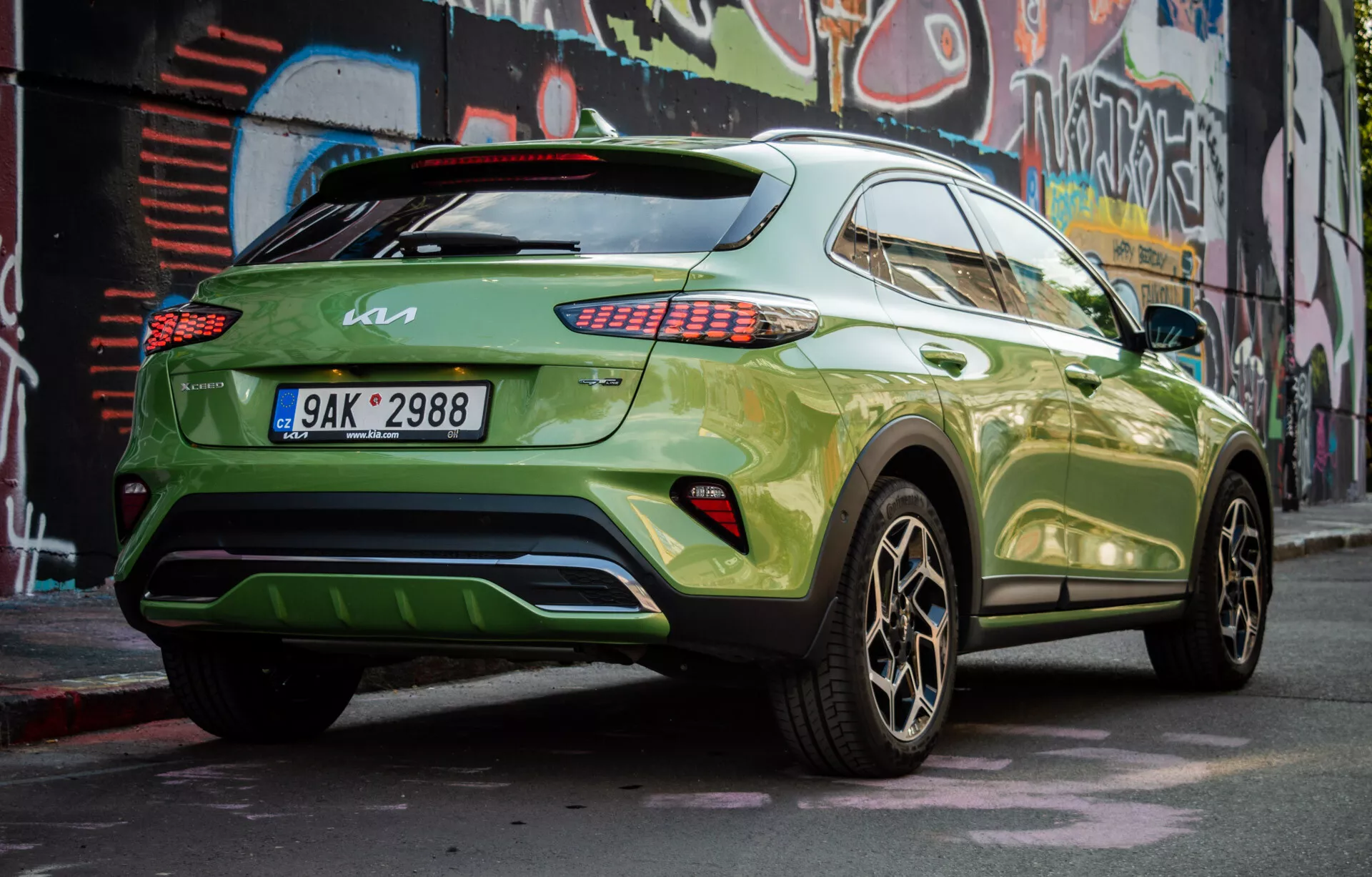 Moderné crossover SUV Kia XCeed 2022 zaparkované diagonálne, ukazujúce jeho pravú zadnú štvrtinu, s výraznou zelenou farbou a tmavými zliatinovými kolesami, demonstruje bočný profil vozidla, zadný dizajn, LED zadné svetlá, tónované okná, spoiler na streche a potenciálny zadný difúzor