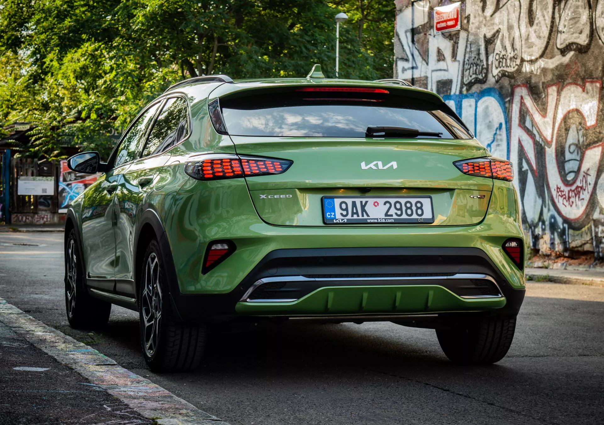 Zadný pohľad na zelený crossover/SUV Kia XCeed 2022 ukazujúci značenie, dizajn LED zadných svetiel, umiestnenie evidenčnej značky, estetiku spodného nárazníka a lesklý povrch na mestskú ulicu.