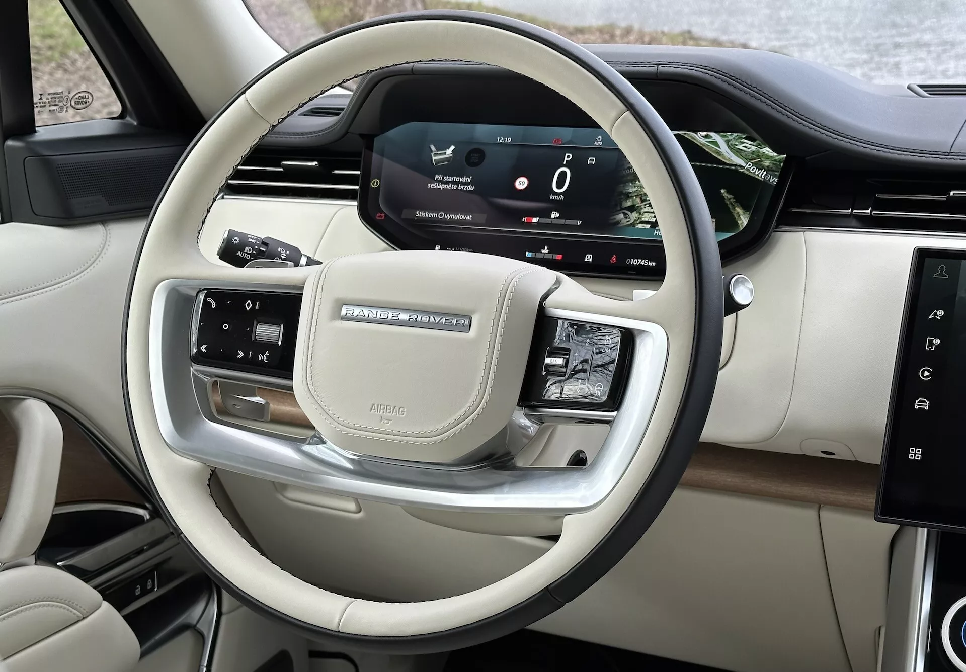 Pohľad na interiér Land Rover Range Rover 2021 s dôrazom na ovládanie na volante a digitálny prístrojový panel vodiča s chrómovými prvkami a luxusnými povrchmi