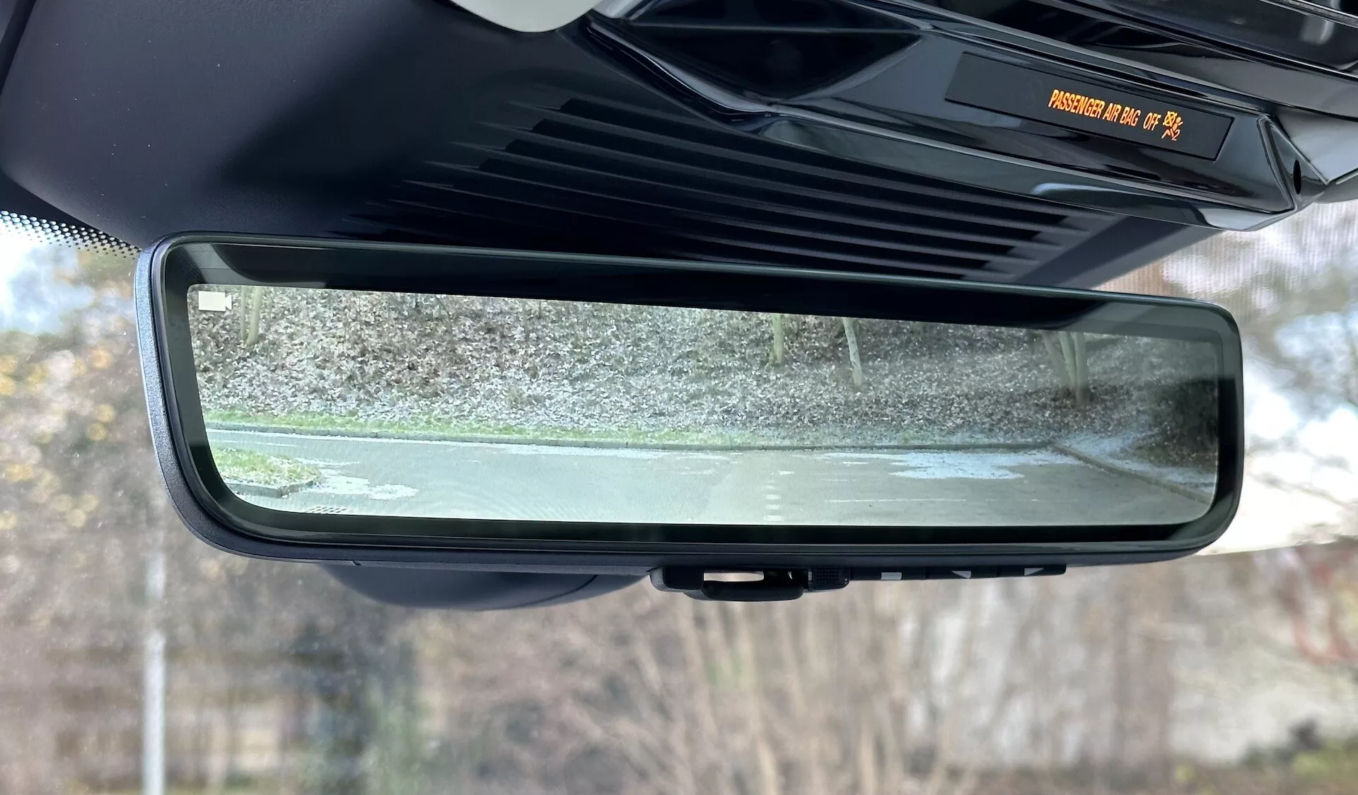 Detailný pohľad na elektrochromatické automaticky stmavovacie spätné zrkadlo vo vnútri Range Rovera 2021, ktoré zdôrazňuje jeho bezrámikový dizajn, prvky interiéru kabíny a odrazenú scénu statického vonkajšieho prostredia